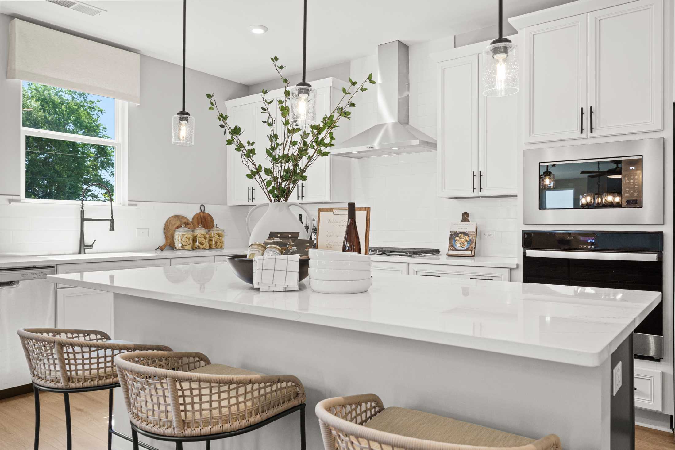 Modern kitchen in The Hickory A by Davidson Homes, Hoschton GA, with white cabinets, large island, rattan stools, and stainless appliances