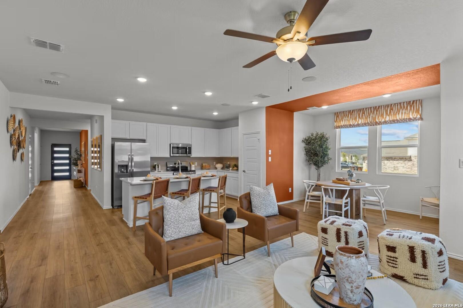 Open-concept kitchen and living room with white cabinets, stainless appliances, leather chairs in Davidson Homes The Daphne K, Bricewood, San Antonio