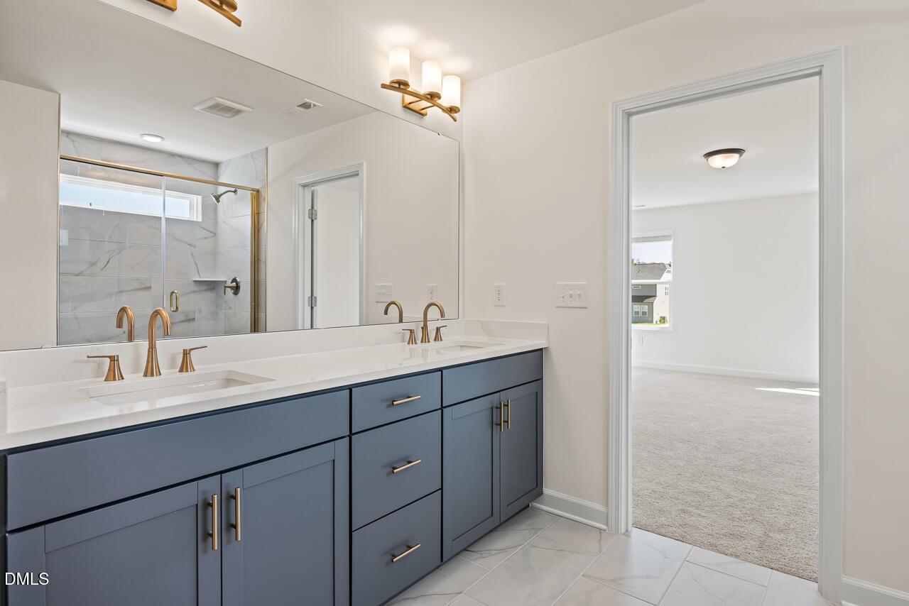 Double vanity bathroom with navy cabinets, gold fixtures, and marble tile in Davidson Homes The Hickory II B, Lillington, NC
