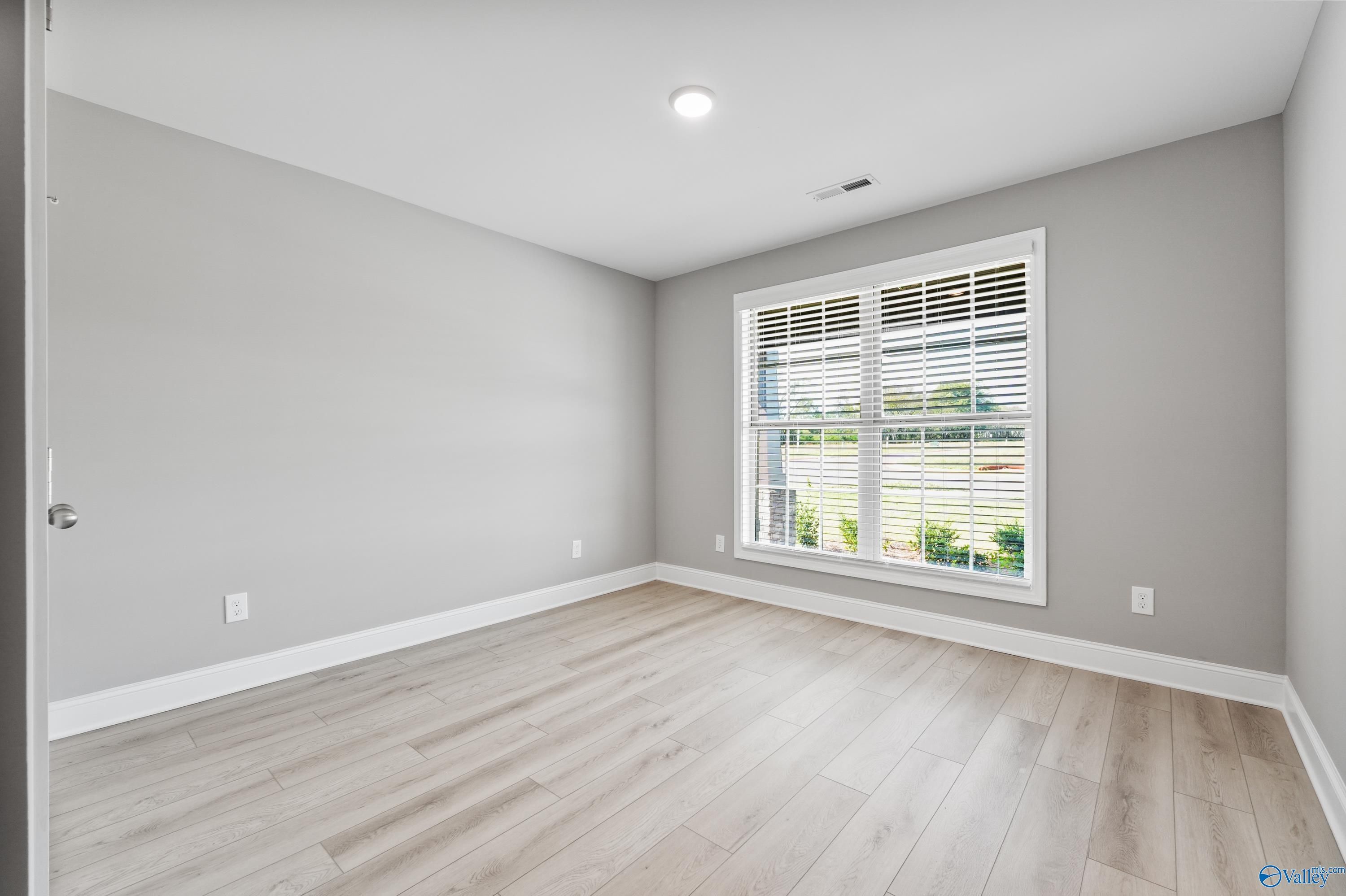 Bright secondary bedroom featuring gray walls, large window with blinds, and light laminate flooring in Davidson Homes The Everett B, Athens AL