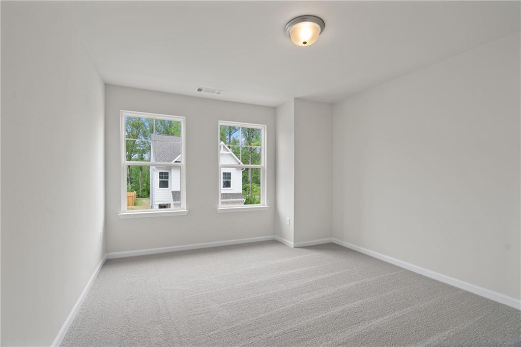Bright bedroom with large double windows overlooking trees, gray carpet, and white walls in Davidson Homes The Marion B, Kennesaw