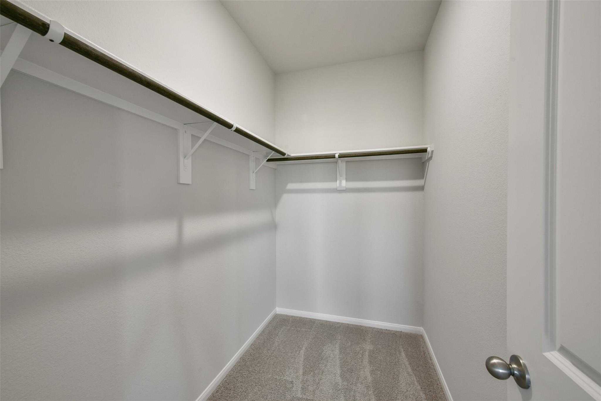 Spacious walk-in closet with wooden shelving, white walls, and carpet floor in Davidson Homes The Sabine E, Dayton, Texas