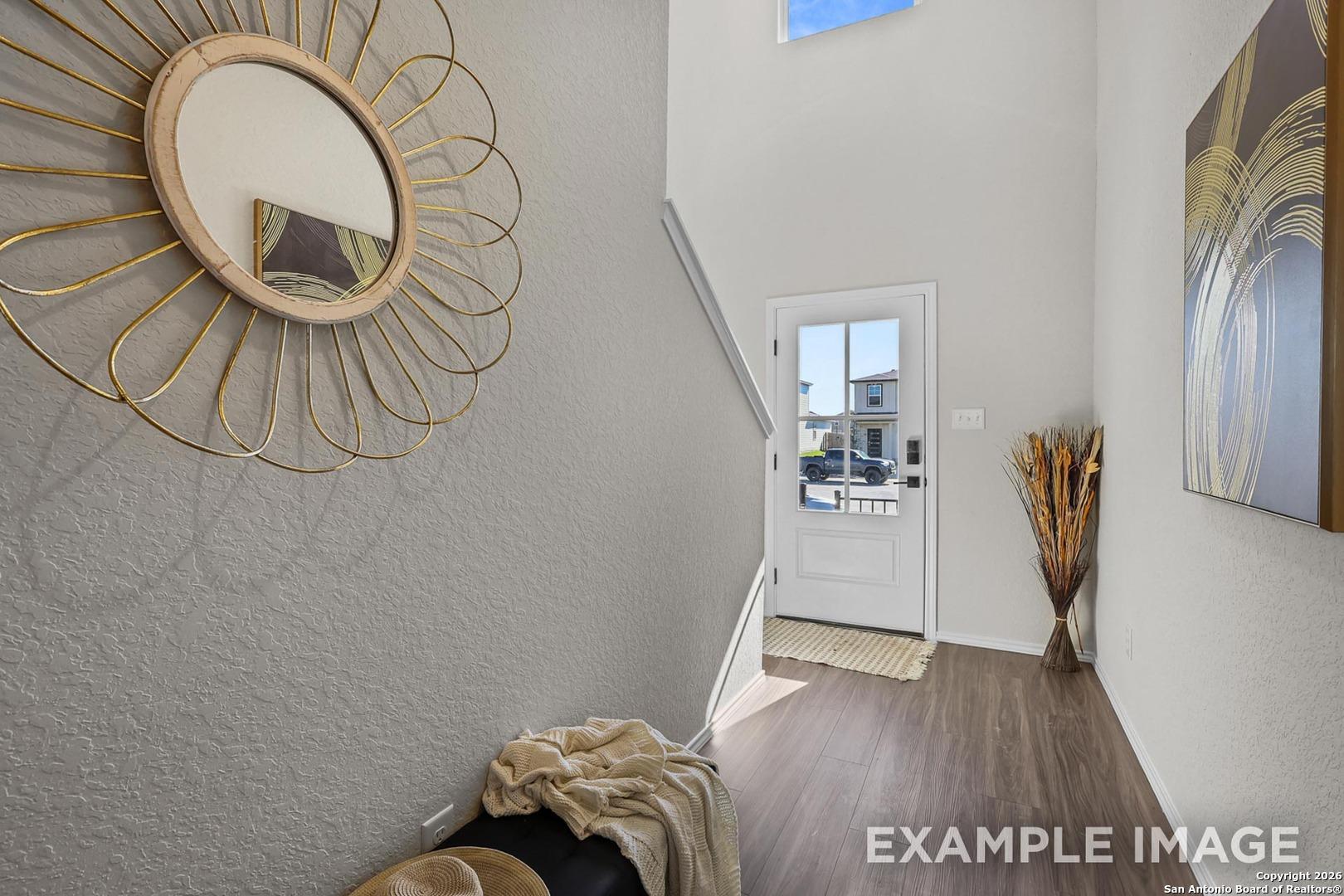 Elegant entry foyer with gold rattan mirror, cushioned bench, skylight, and abstract art in Davidson Homes The Trinity B, San Antonio