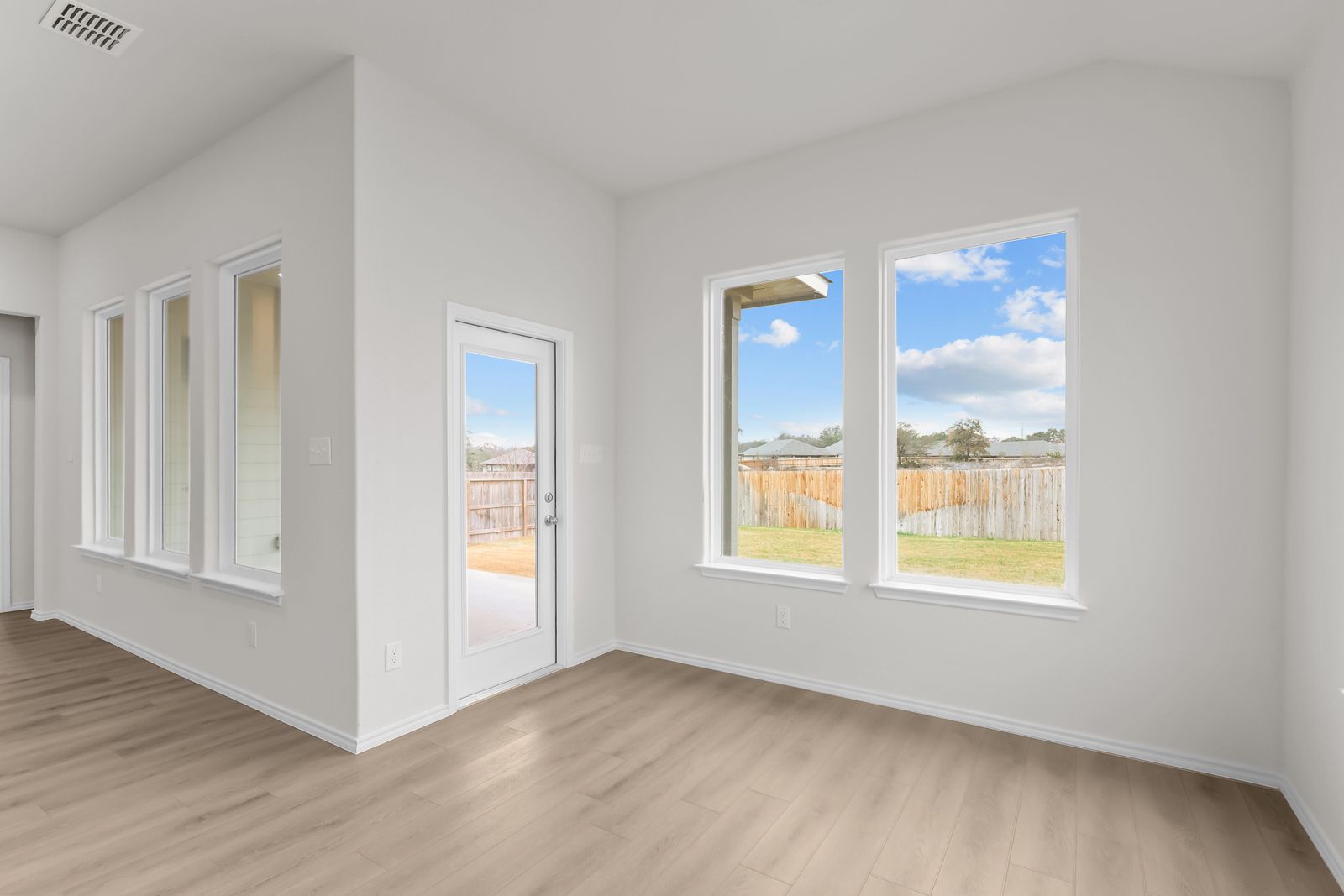 Bright living area in The Sequoia C featuring large windows, wood-style flooring, and backyard access in Converse, Texas.