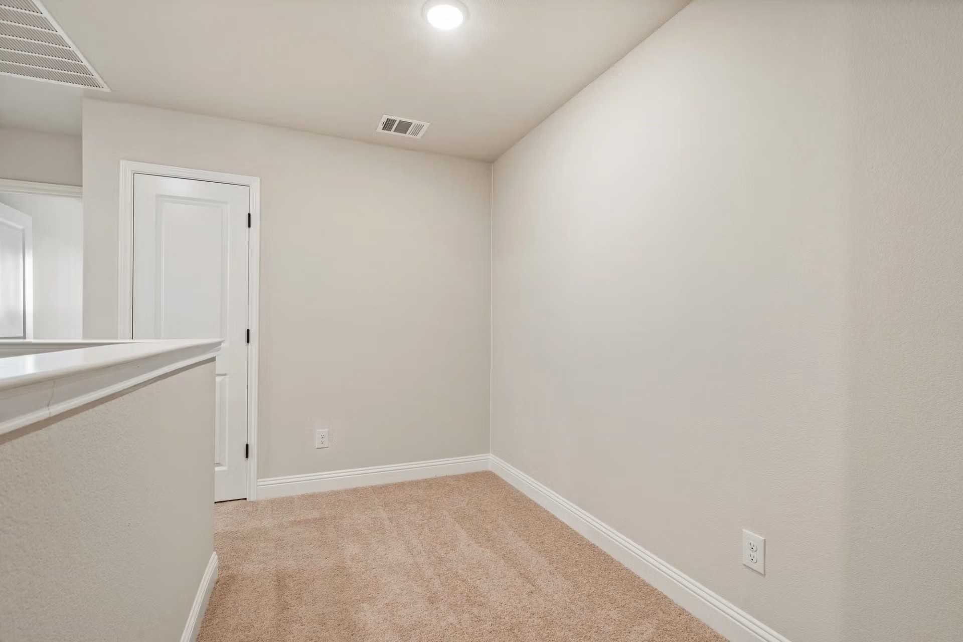 Spacious upstairs loft with beige walls, carpeted floor, and white railing in Davidson Homes The Wake D, Wylie Texas