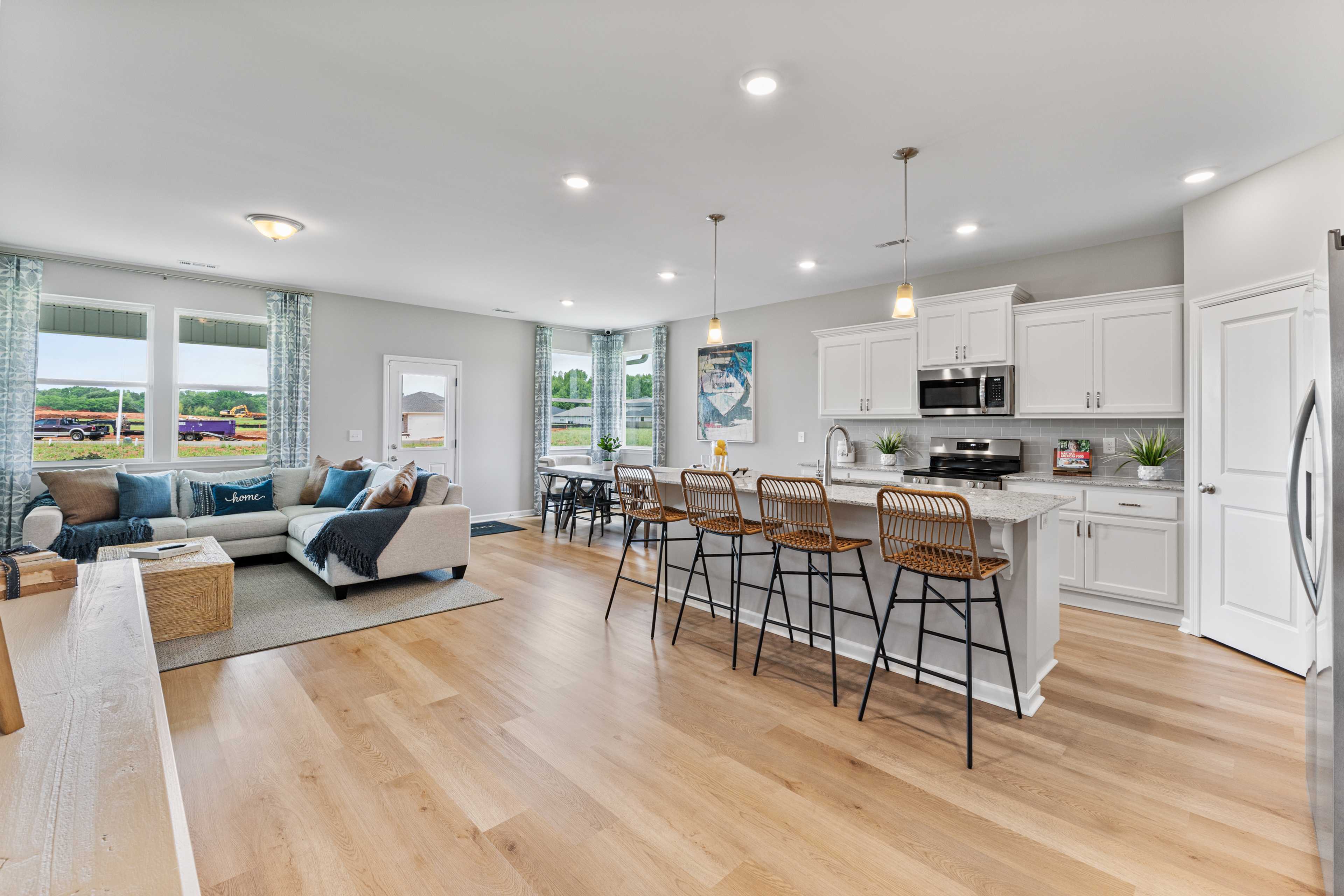 Open-concept living kitchen in Forest Glen Hazel Green AL with hardwood floors white cabinets island bar stools and large windows