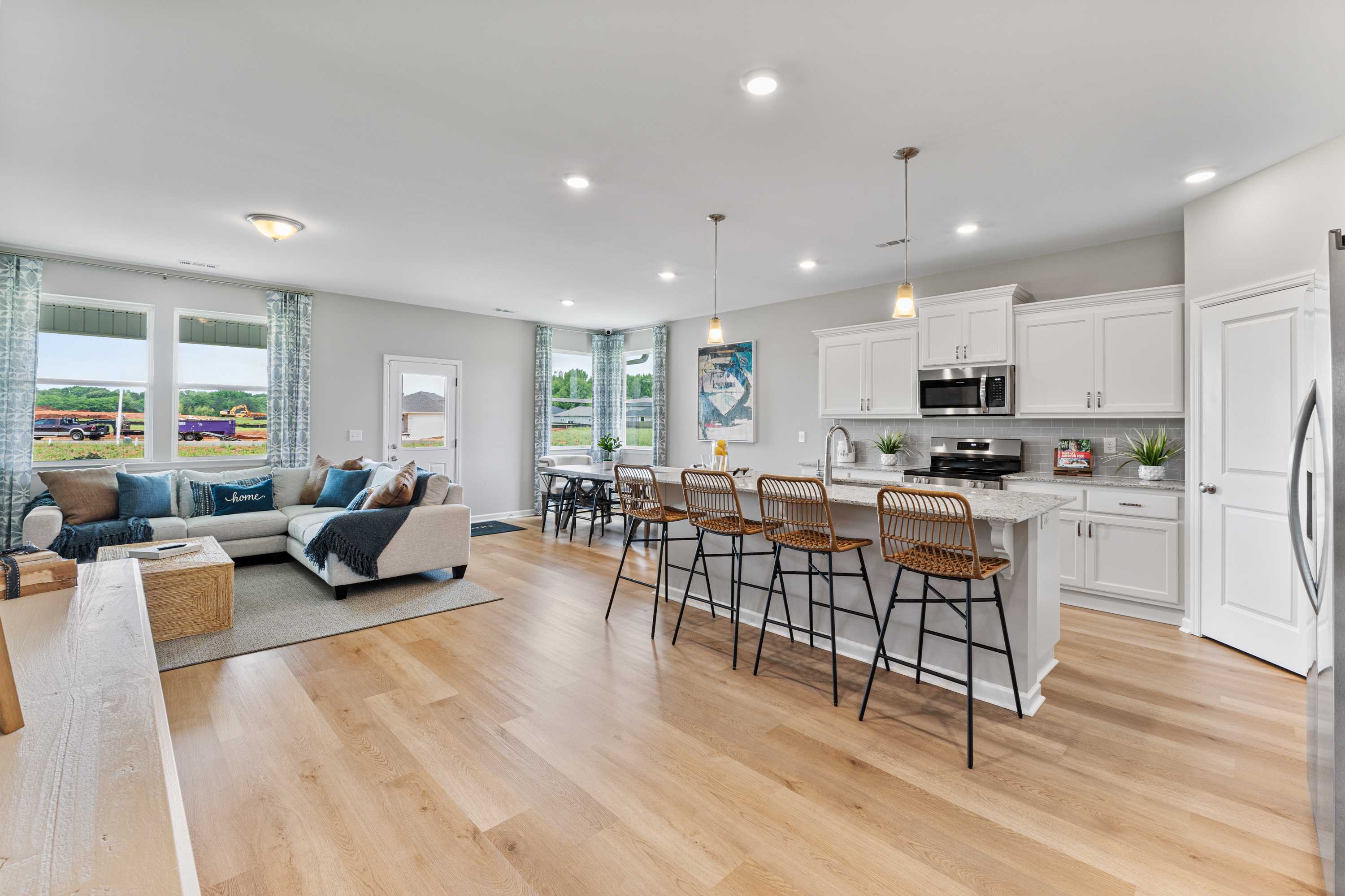 Open-concept living kitchen in Forest Glen Hazel Green AL with hardwood floors white cabinets island bar stools and large windows