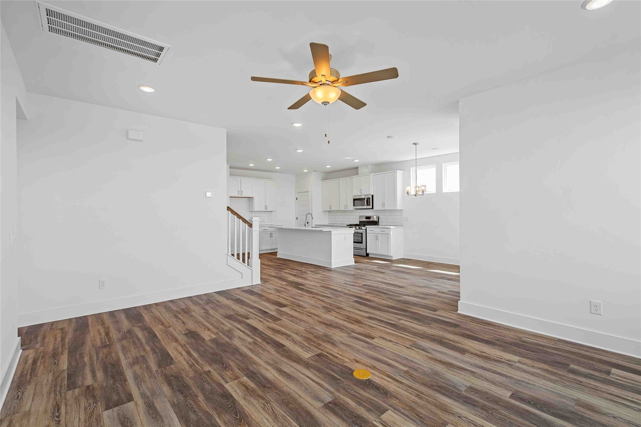 Open-concept floor plan with white kitchen, island, and wood-look flooring in The Ash O by Davidson Homes, Heartland, TX.