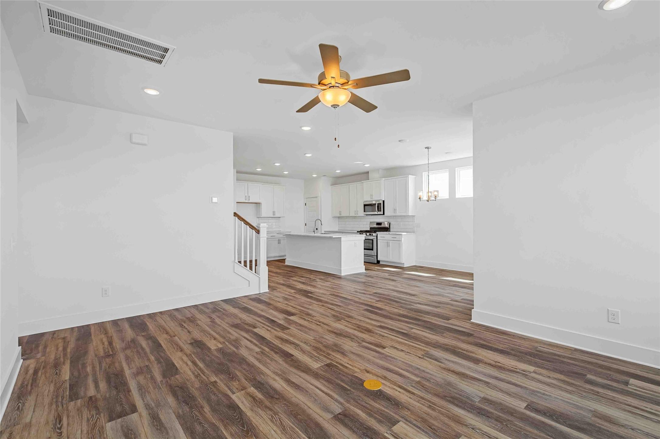 Open-concept floor plan with white kitchen, island, and wood-look flooring in The Ash O by Davidson Homes, Heartland, TX.