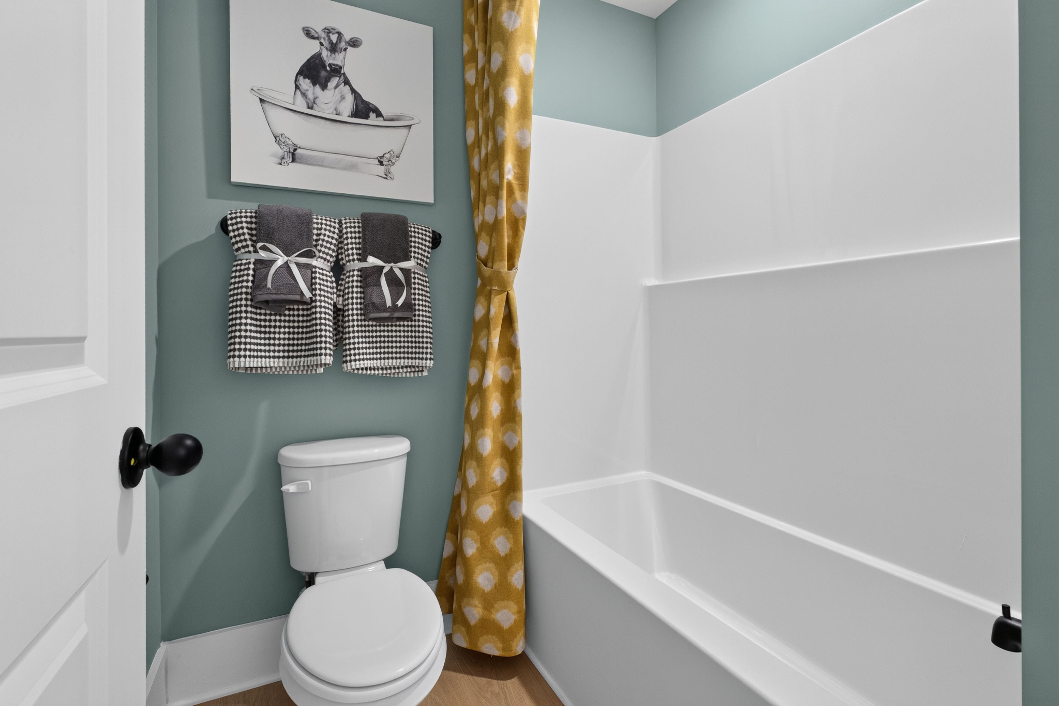 Bathroom with sage green walls, white tub and toilet at Evergreen Mill by Davidson Homes in Madison, Alabama