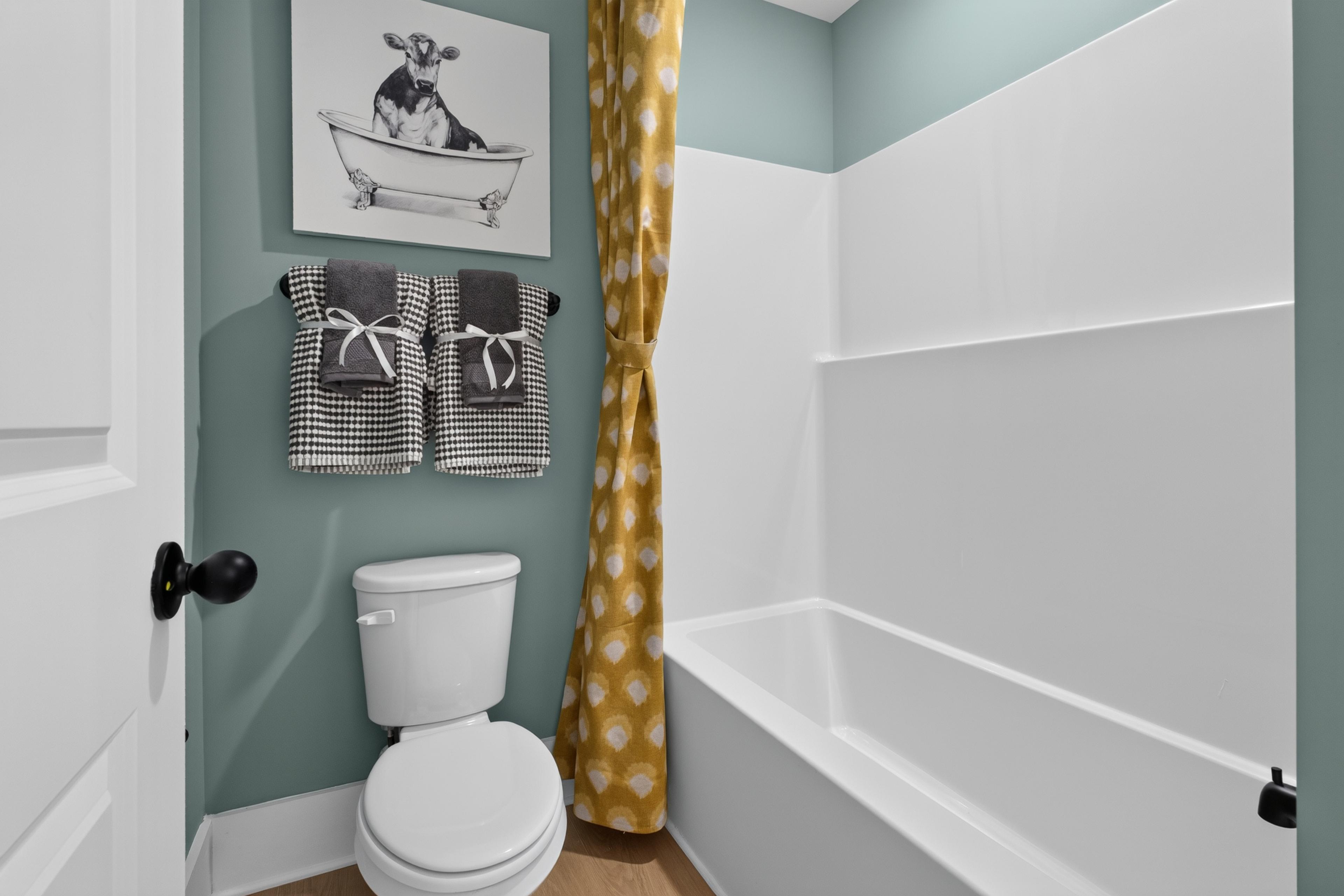 Bathroom with sage green walls, white tub and toilet at Evergreen Mill by Davidson Homes in Madison, Alabama