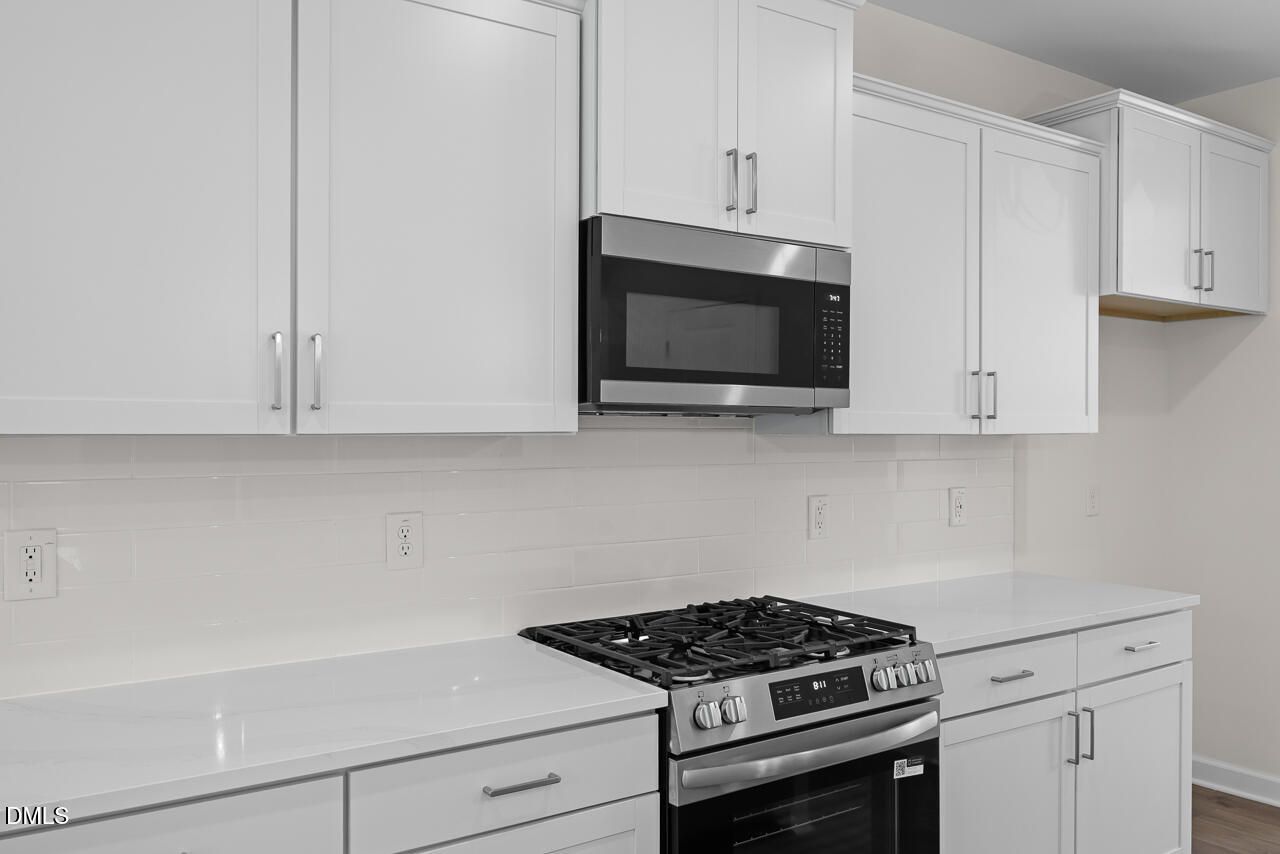 Modern kitchen with white shaker cabinets, gas range, microwave, and quartz countertops in Davidson Homes Willow B, Zebulon NC