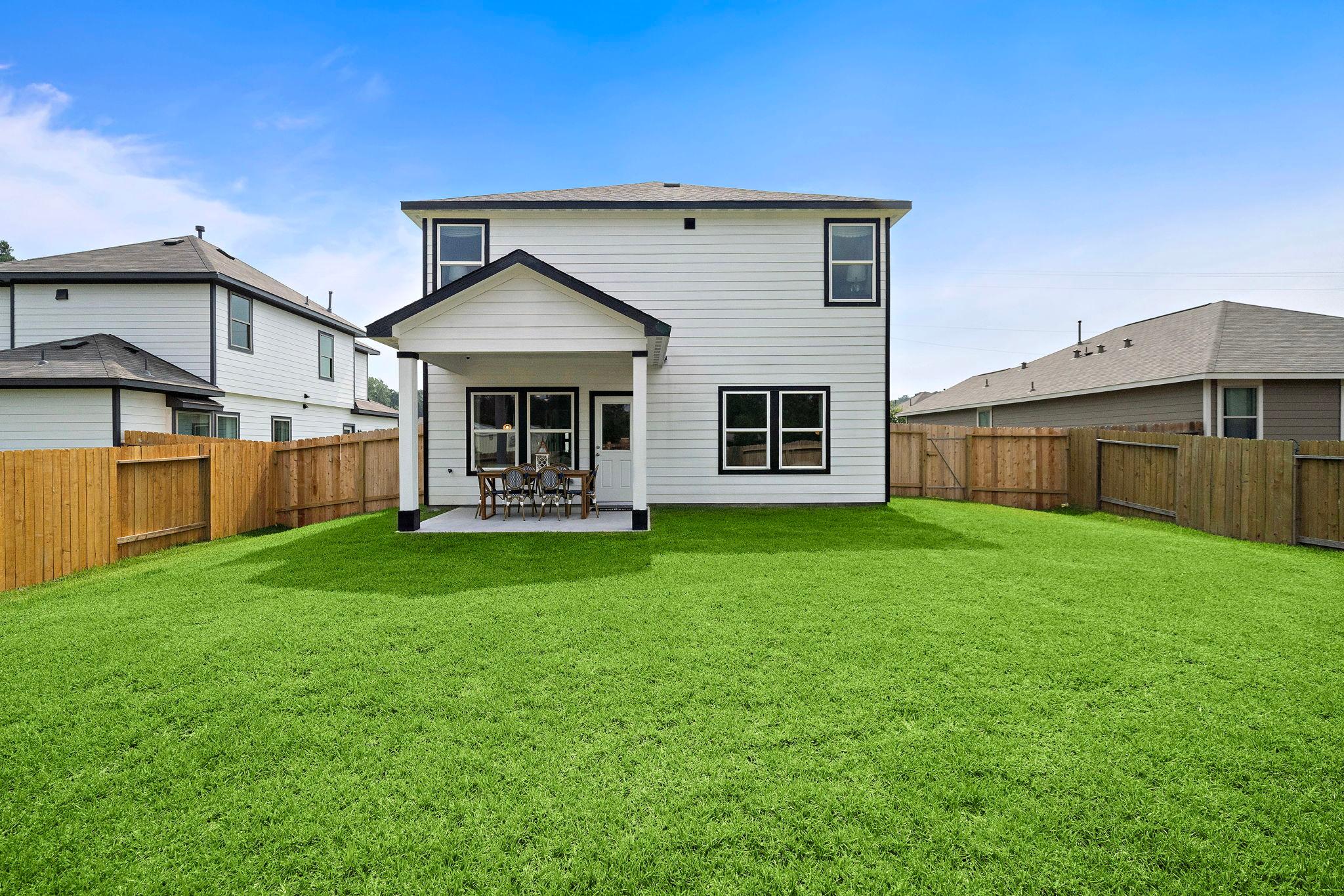 Spacious backyard with covered patio at Liberty Estates in Cleveland Texas by Davidson Homes featuring lush green lawn and outdoor seating