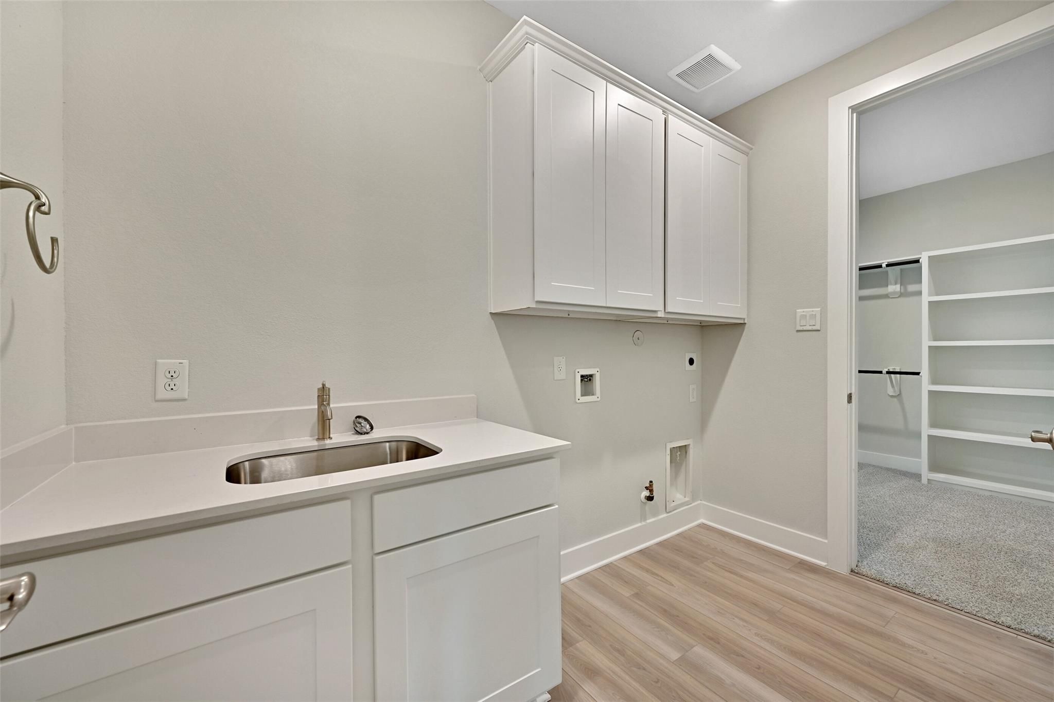 Modern laundry room featuring white shaker cabinets, stainless utility sink, and washer-dryer hookups in Davidson Homes The Edward A, Lago Mar, Texas City