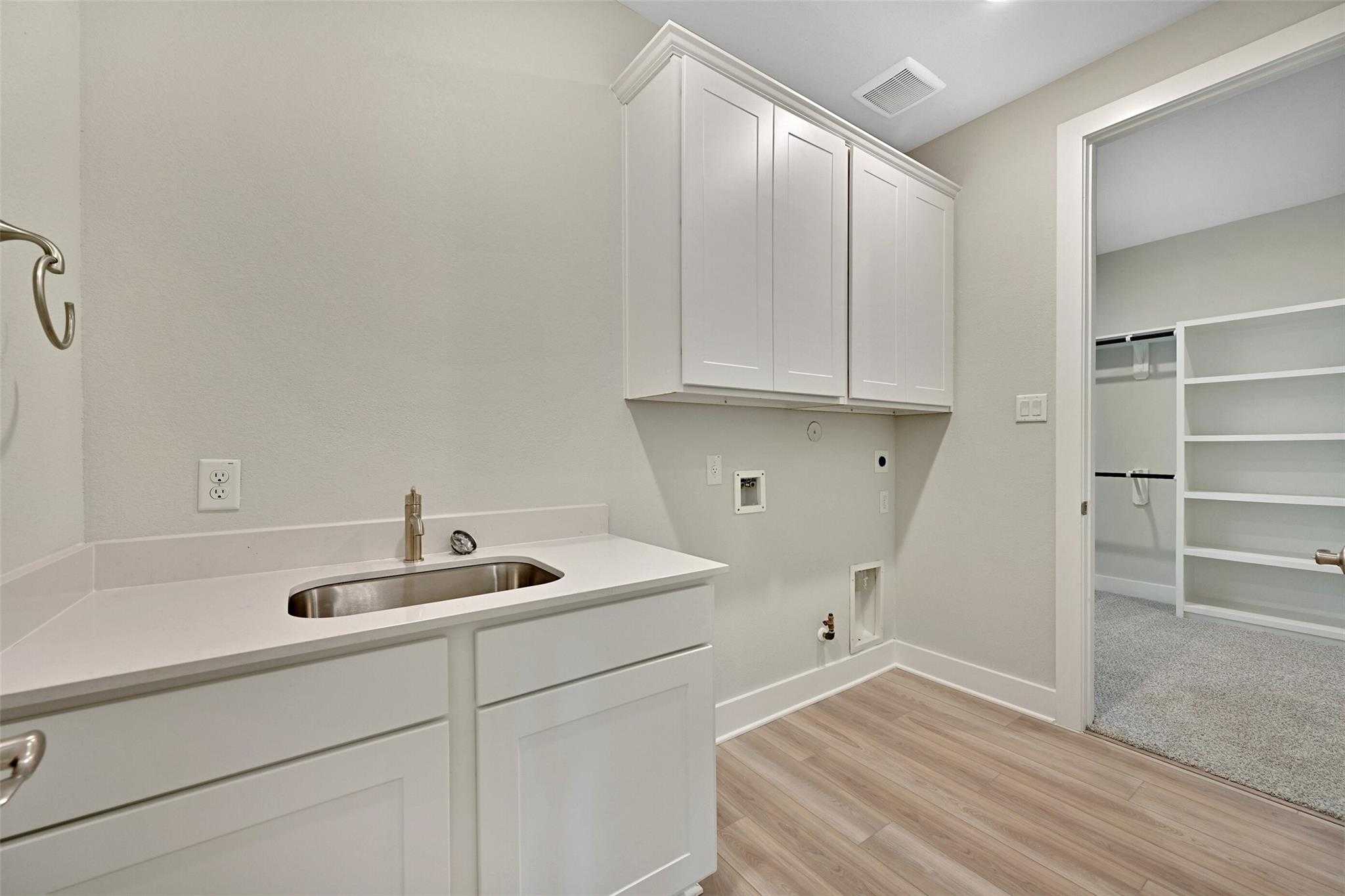 Modern laundry room with white shaker cabinets, deep stainless sink, and adjacent storage closet in Davidson Homes The Edward A, Lago Mar, Texas City