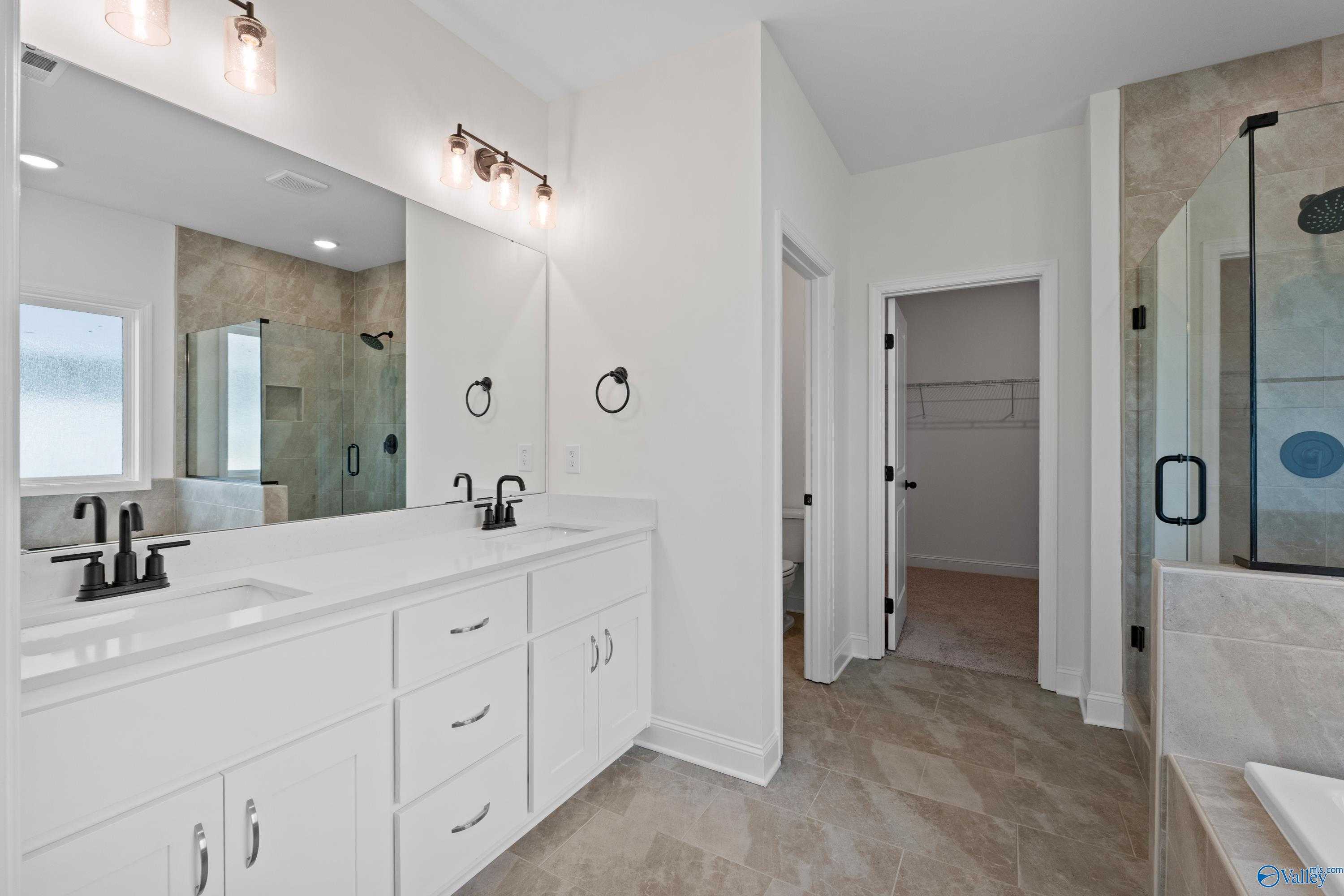 Modern master bathroom featuring double white vanity, glass shower, and closet door in Davidson Homes The Rockford B, Toney, Alabama