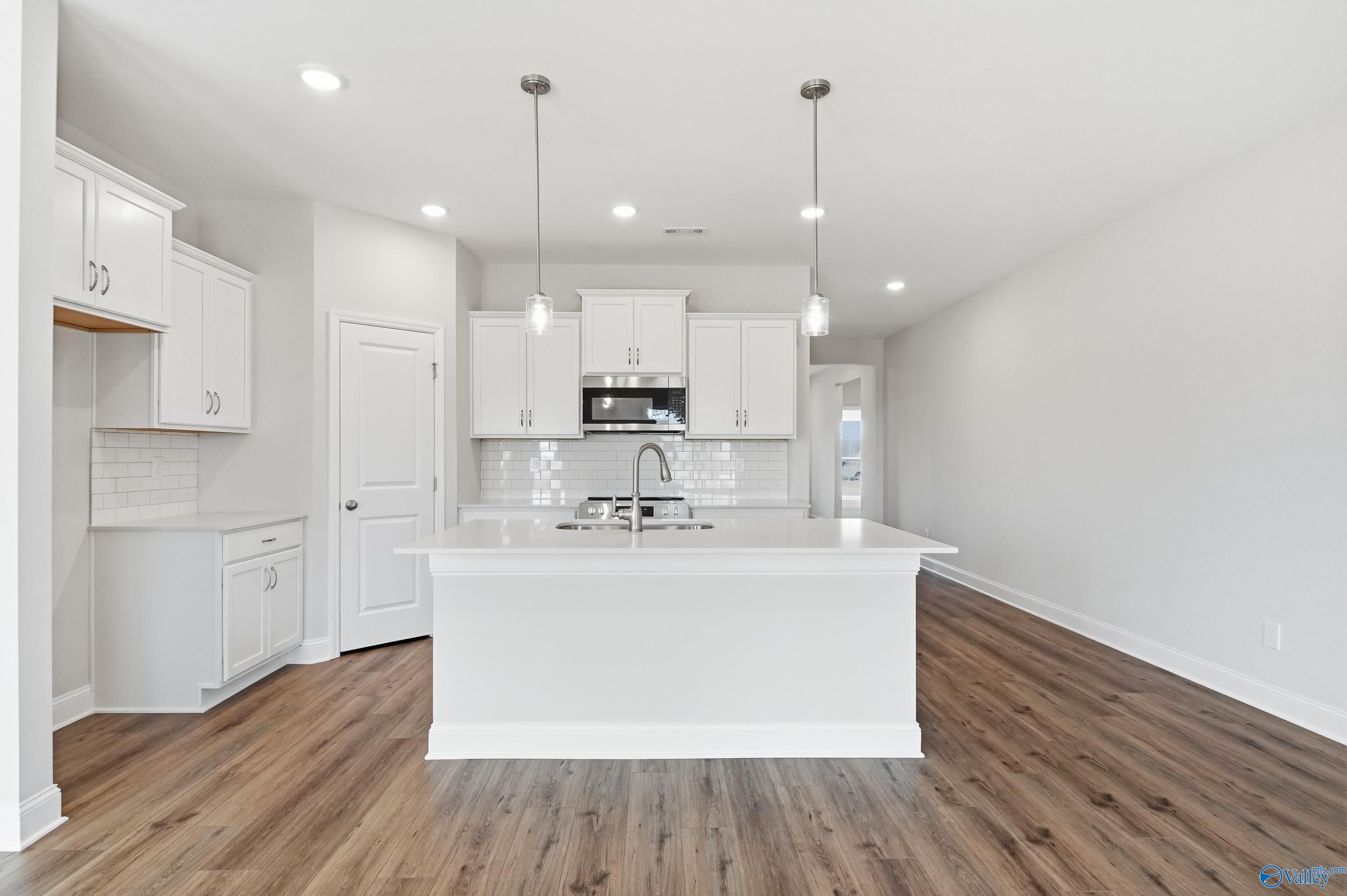 Modern white kitchen island with stainless appliances, subway tile backsplash, and hardwood floors in Davidson Homes The Daphne C, Toney, AL