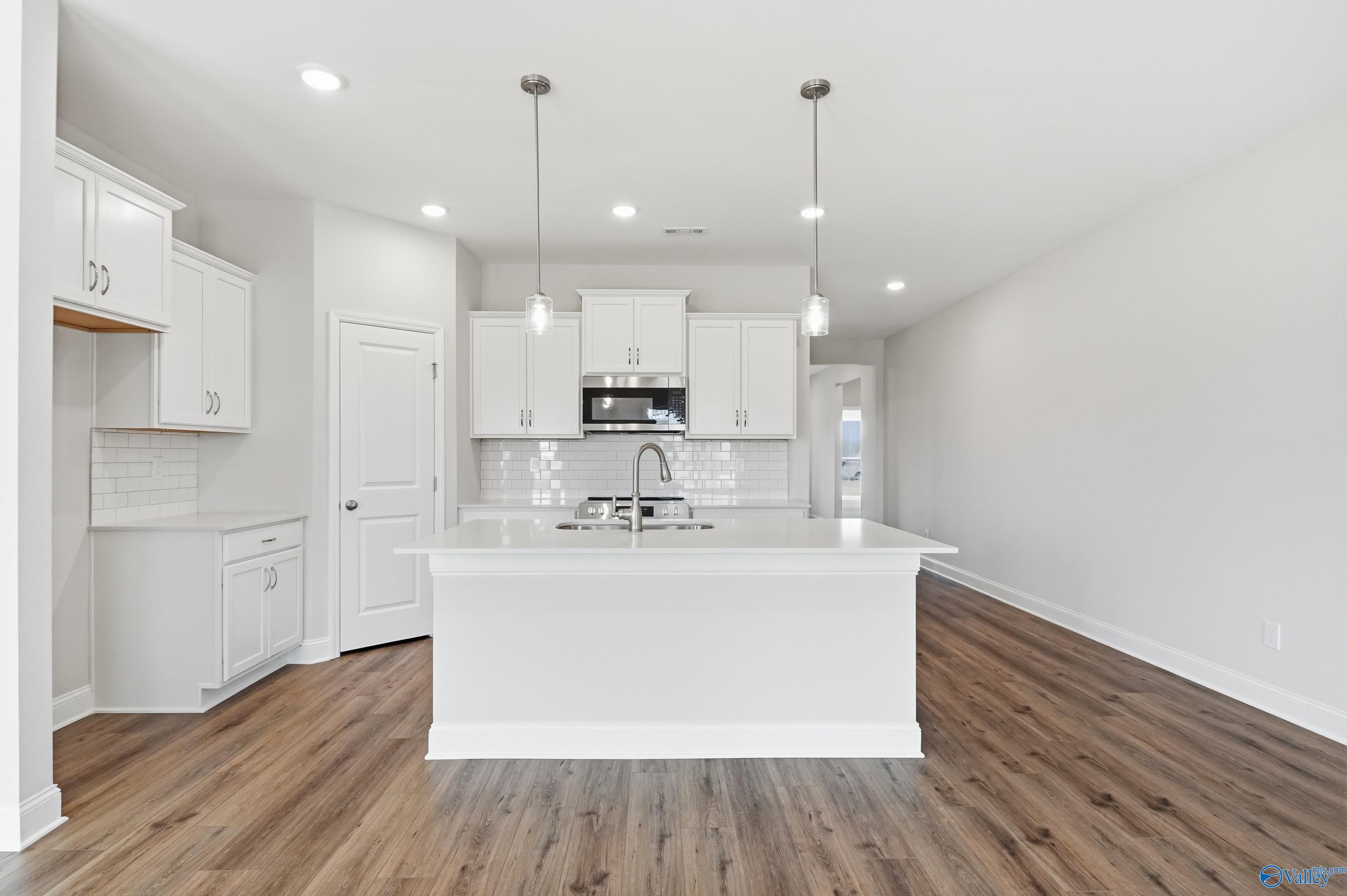 Modern white kitchen island with stainless appliances, subway tile backsplash, and hardwood floors in Davidson Homes The Daphne C, Toney, AL
