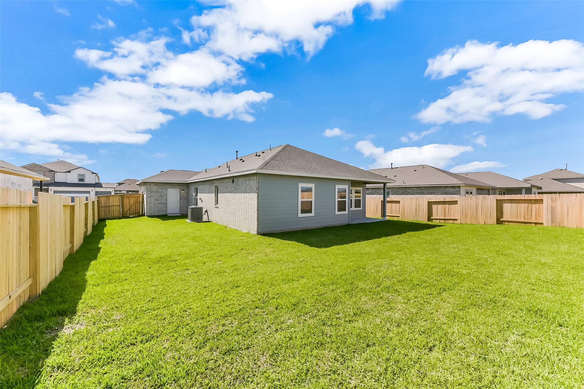 Expansive lush green backyard with wooden privacy fences behind single-story gray home in River Ranch Meadows, Dayton, Texas