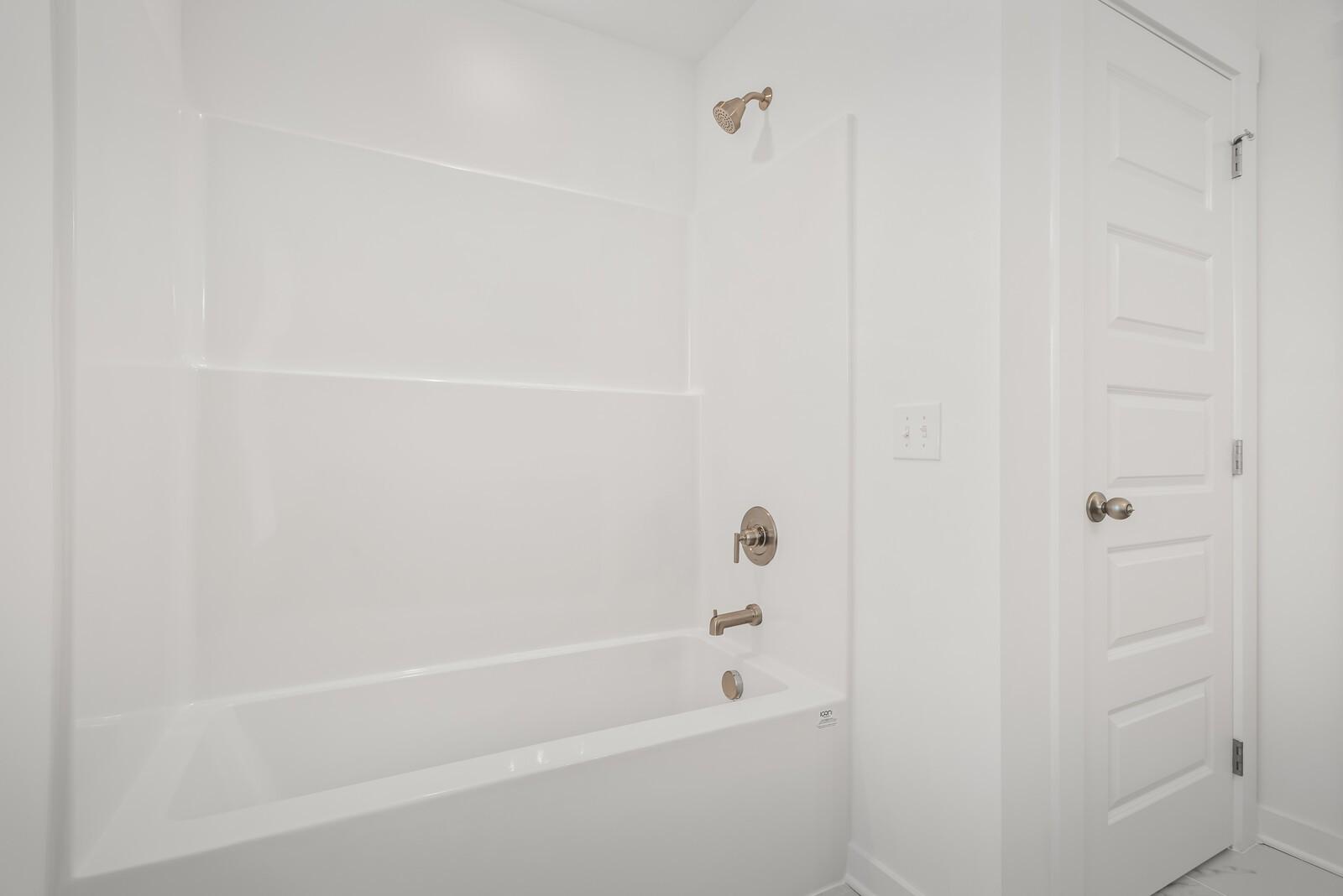 Modern white bathroom with tiled shower, freestanding tub, brass fixtures in Davidson Homes The Gordon C, White House, TN
