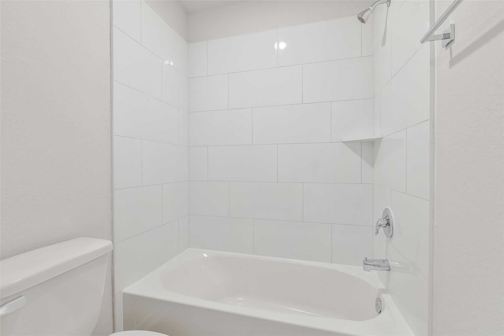 Modern white subway tile bathroom with deep soaking tub, shower, and toilet in Davidson Homes The Trinity F, Magnolia TX