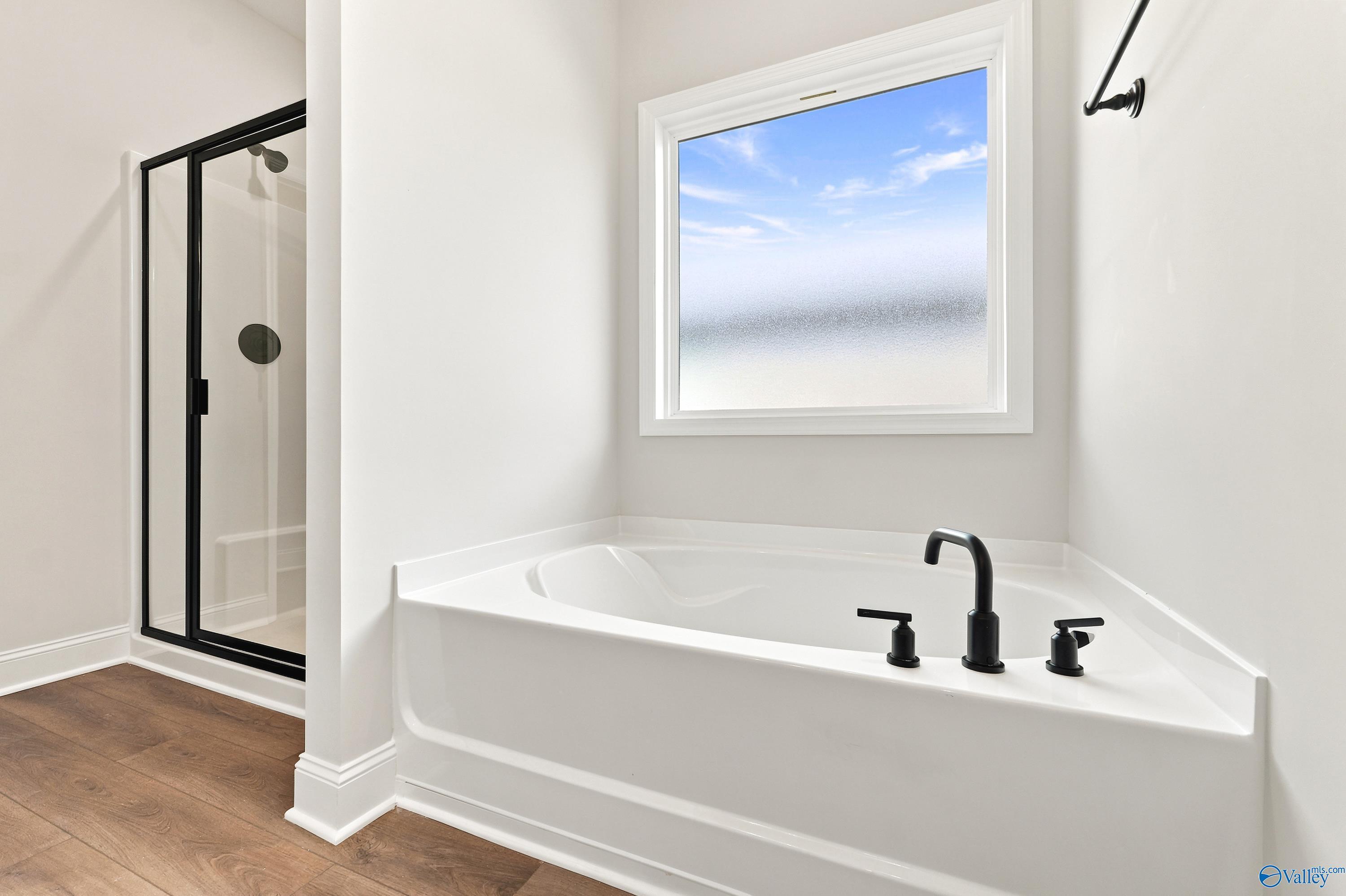 Modern master bathroom with soaking tub, glass-enclosed shower, and matte black fixtures in The Daphne, Meridianville, AL.