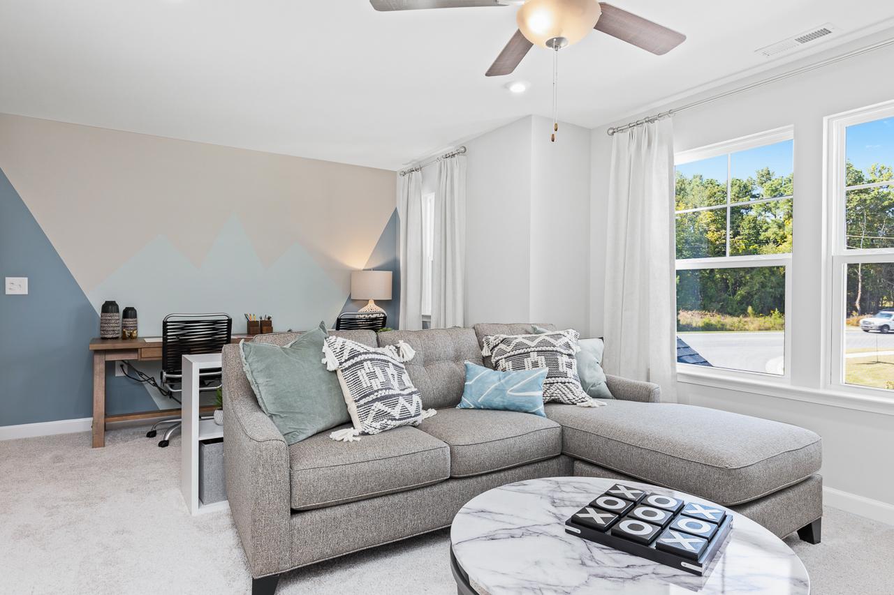 Cozy flex room in The Hemlock A featuring a gray sectional sofa, mountain-themed accent wall, and home office nook.
