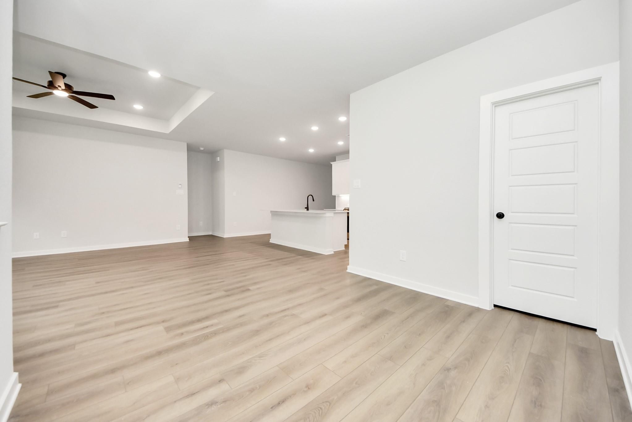 Open-concept living room with tray ceiling and wood-style flooring in The Daphne F floor plan at Sundance Cove, Crosby.