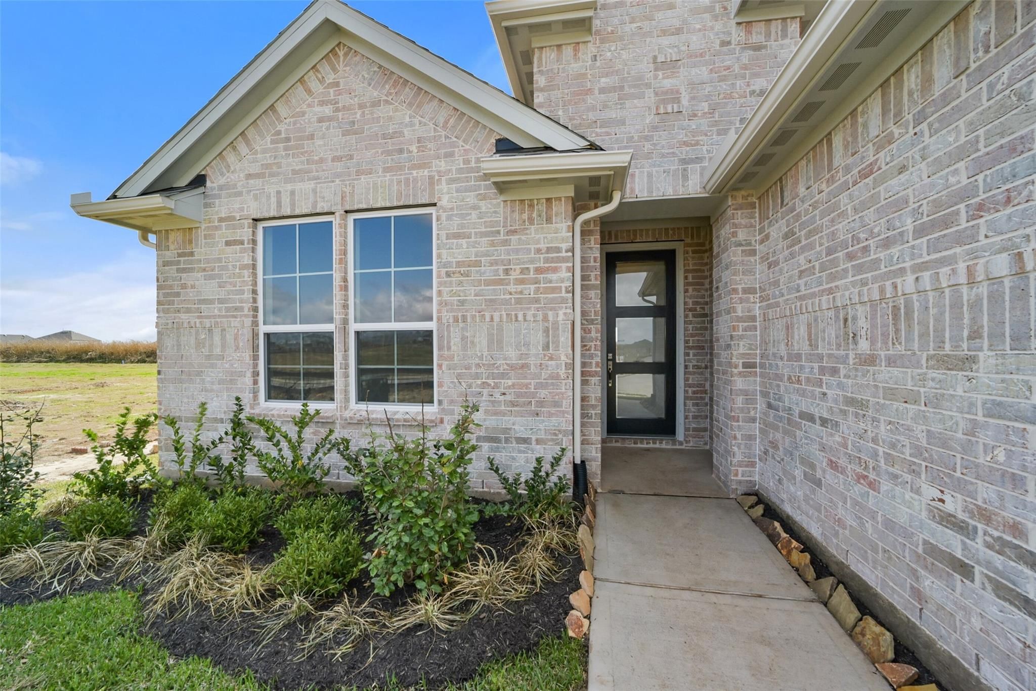 Beige brick two-story home exterior with modern glass door, large windows, and landscaped entry in Davidson Homes Zion A, Lago Mar, Texas City