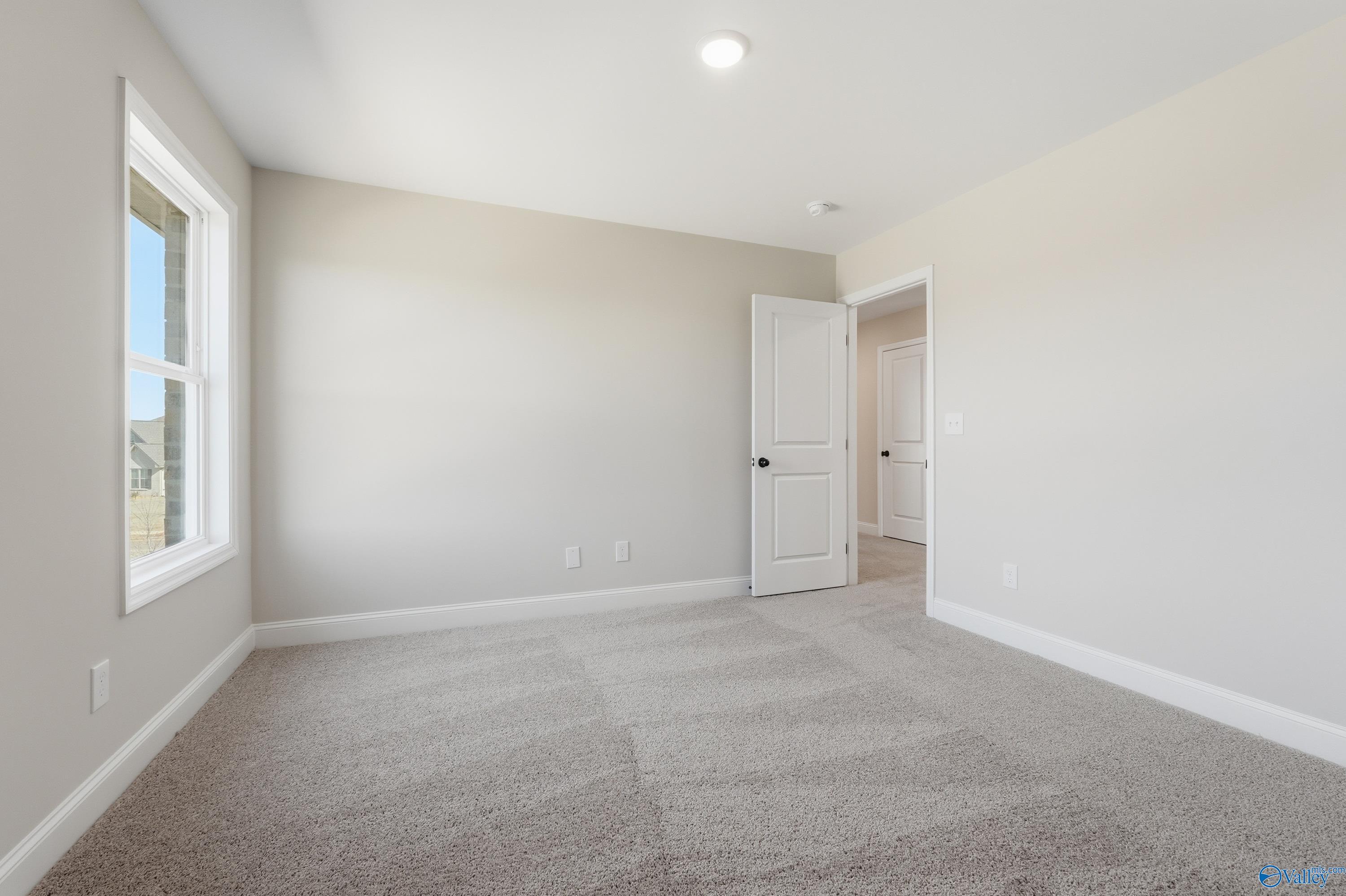 Spacious secondary bedroom with beige walls, plush carpet, large window, and connecting door in Davidson Homes The Chelsea C, Harvest, Alabama