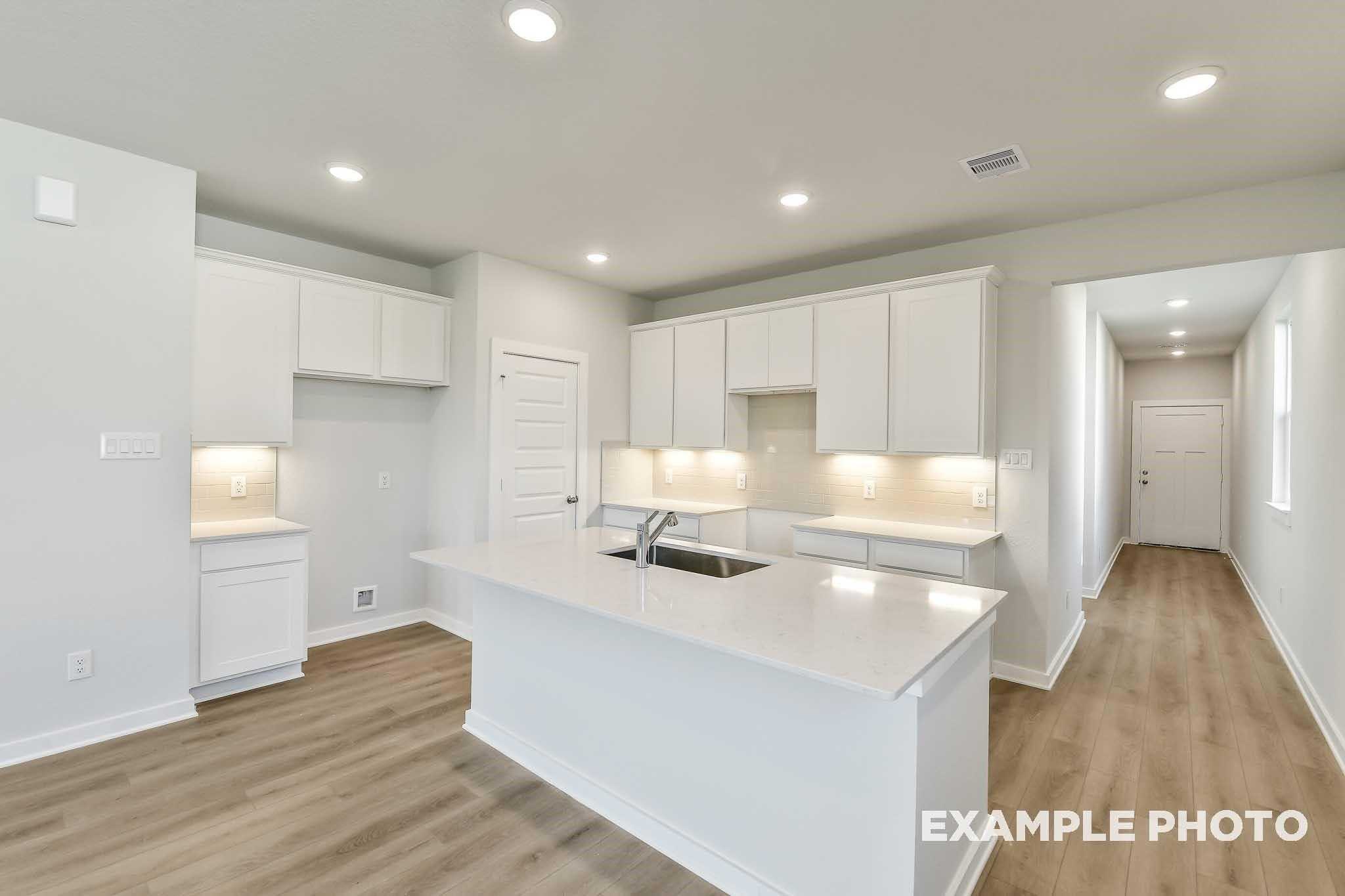 Modern white kitchen with quartz island sink, recessed lighting, and open layout in Davidson Homes The Colorado F, Conroe, Texas