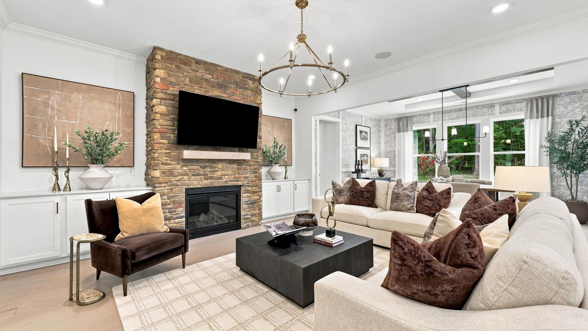 Stylish model home living room with stone fireplace, cream sofas, and chandelier at Davidson Homes' Fall in Love with Rockport event