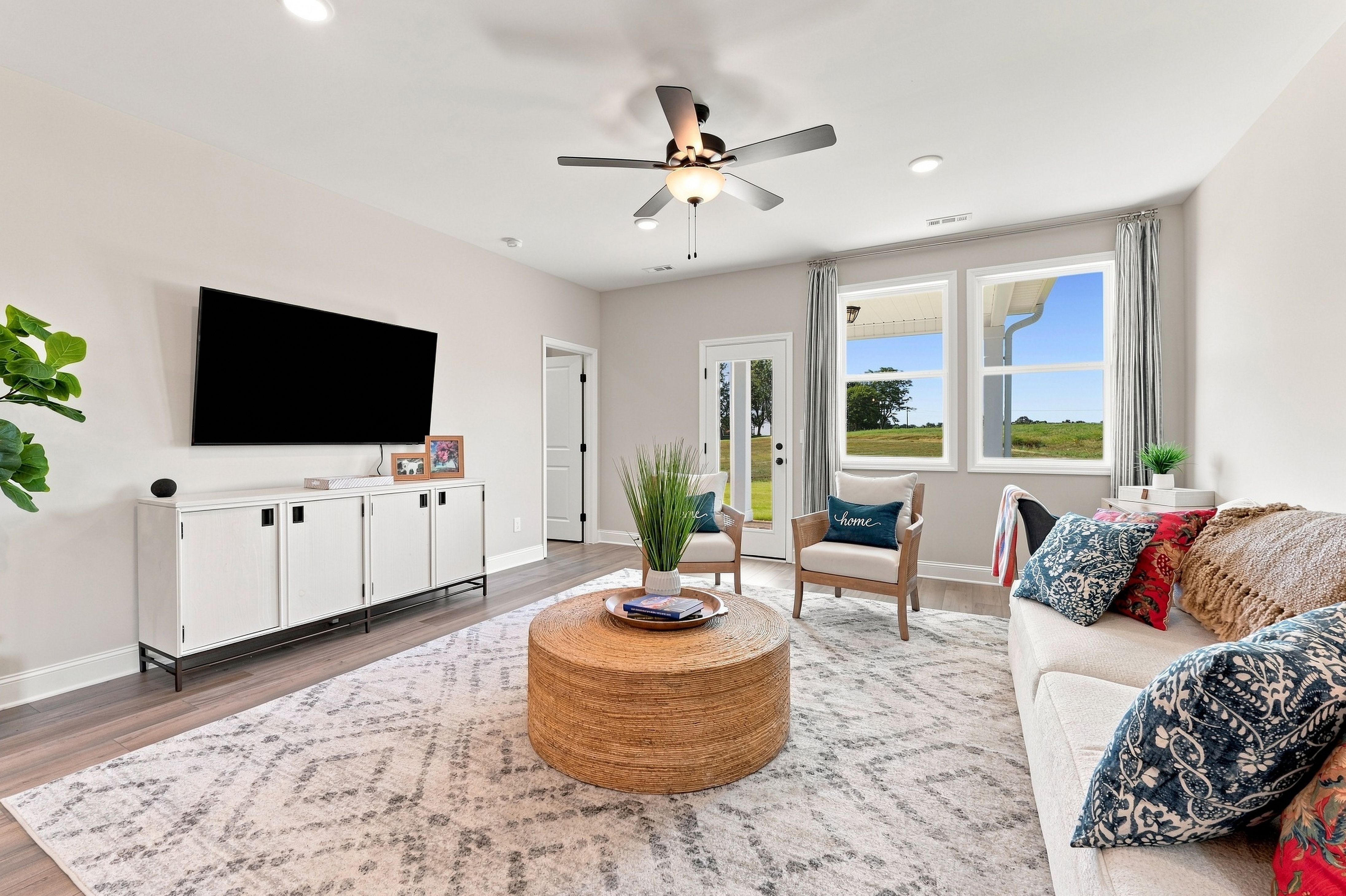 Bright living room at Bailey Park in Fayetteville, TN by Davidson Homes with ceiling fan, round coffee table, and backyard views