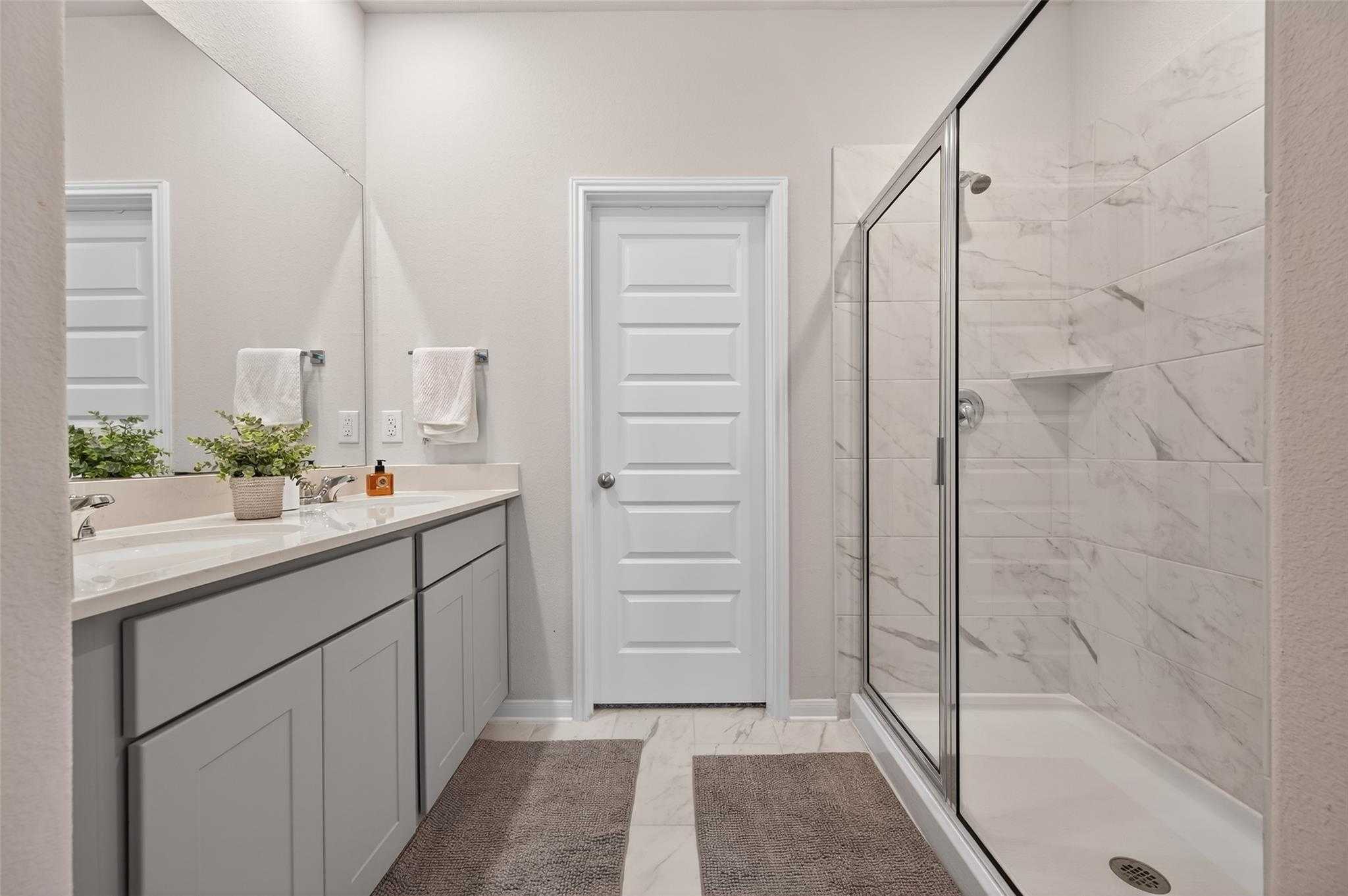 Elegant master bathroom with gray double vanity, frameless glass shower, and subway tile in Davidson Homes The Brazos E, Magnolia, Texas