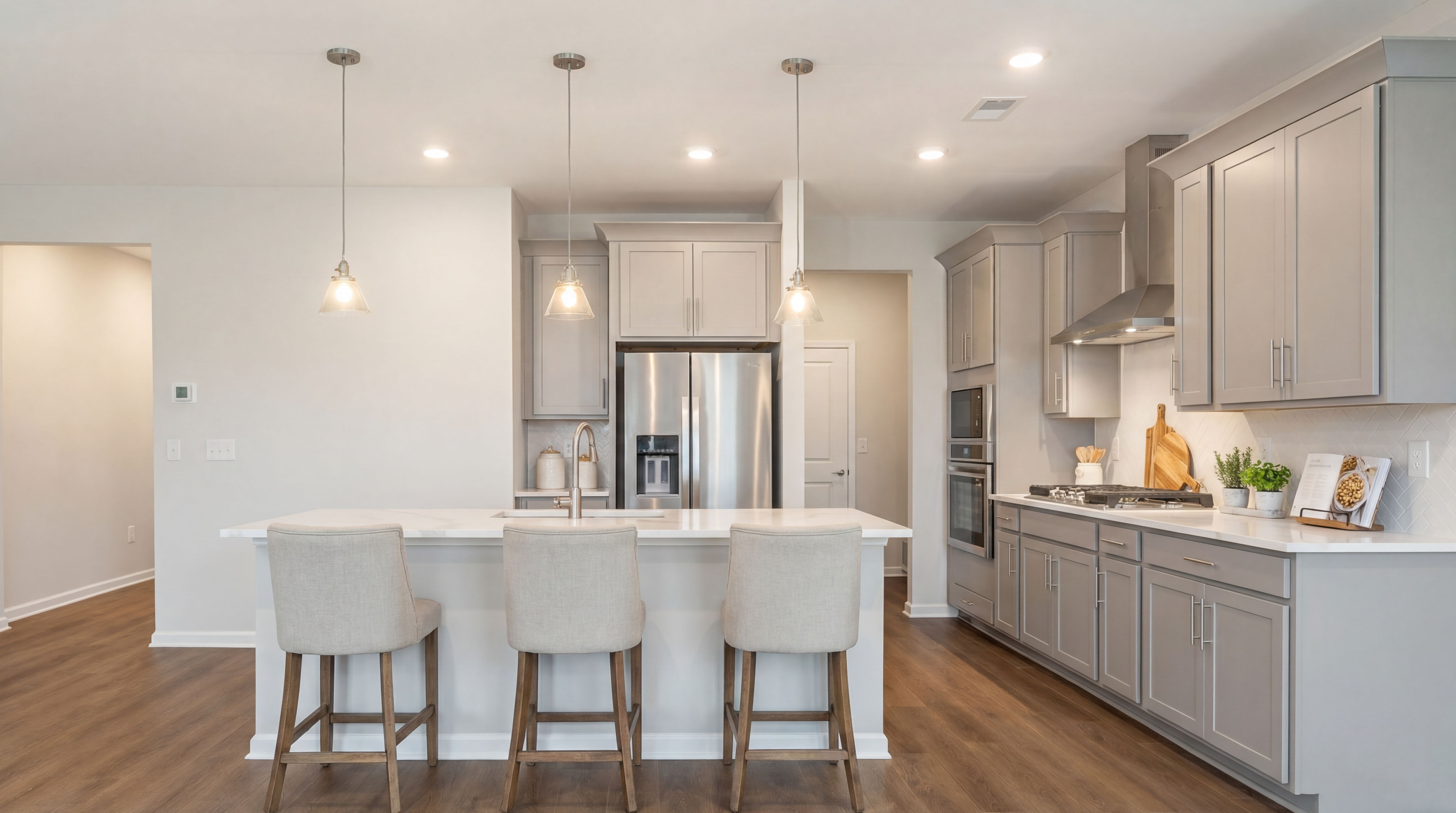 Modern kitchen in Lake Shore Winder GA with white shaker cabinets, large island bar stools, stainless steel appliances, hardwood floors