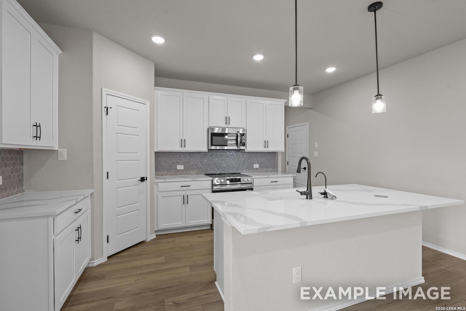 Modern white kitchen with large island, quartz countertops, pendant lights, and hexagon tile backsplash in The Murray H, Converse TX