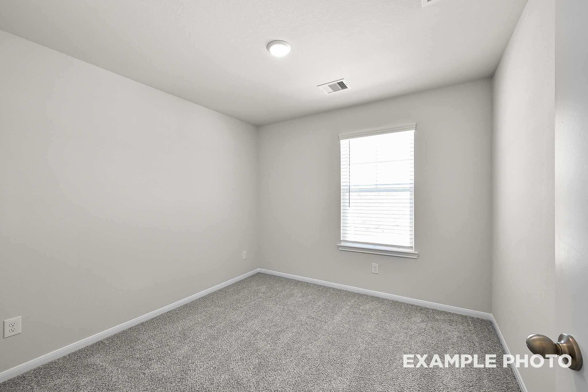 Bright, carpeted bedroom with neutral walls in The Blanco F floor plan at Spring Branch Crossing, Conroe, Texas.