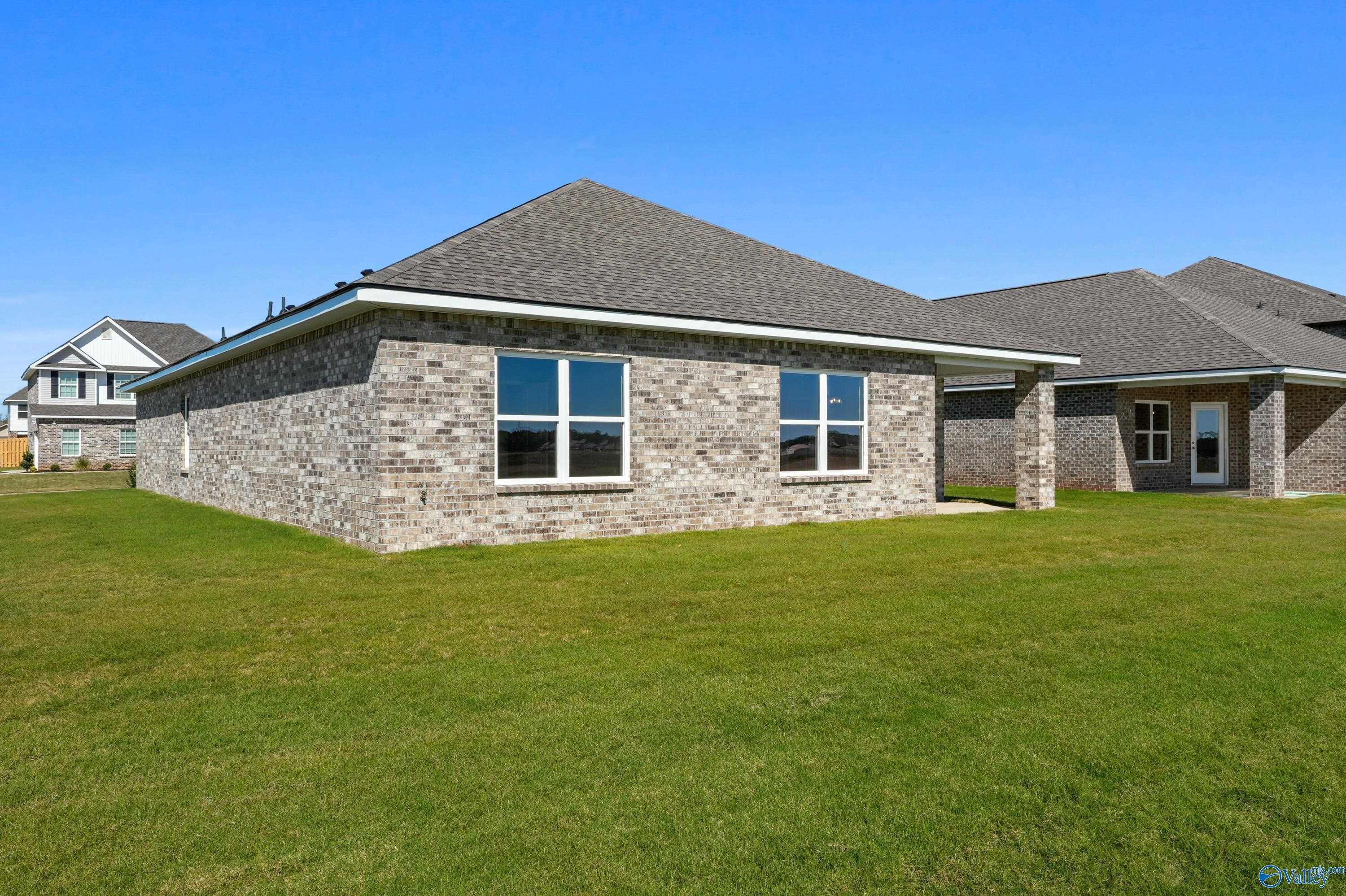 Brick side exterior of The Daphne C 4-bedroom home with 2-car garage, large windows, and lush green lawn in Clearview, Hazel Green, Alabama