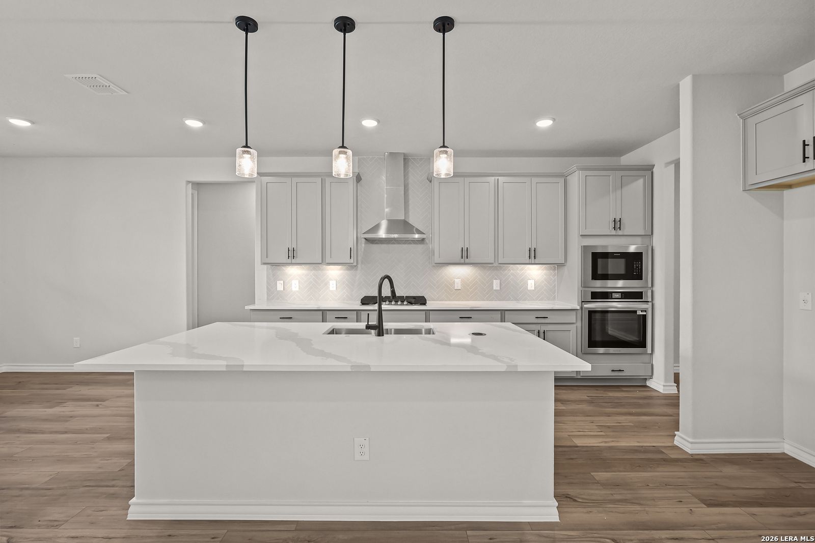 Modern kitchen with large quartz island, gray shaker cabinets, pendant lights, and stainless appliances in Davidson Homes The Oxford F, Castroville