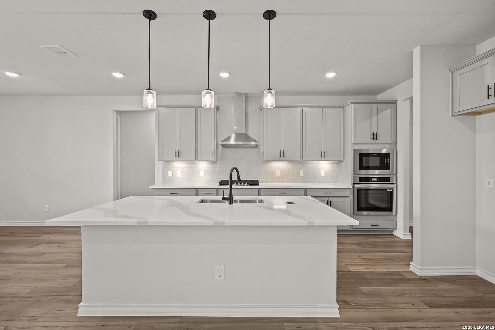 Modern kitchen with large quartz island, gray shaker cabinets, pendant lights, and stainless appliances in Davidson Homes The Oxford F, Castroville