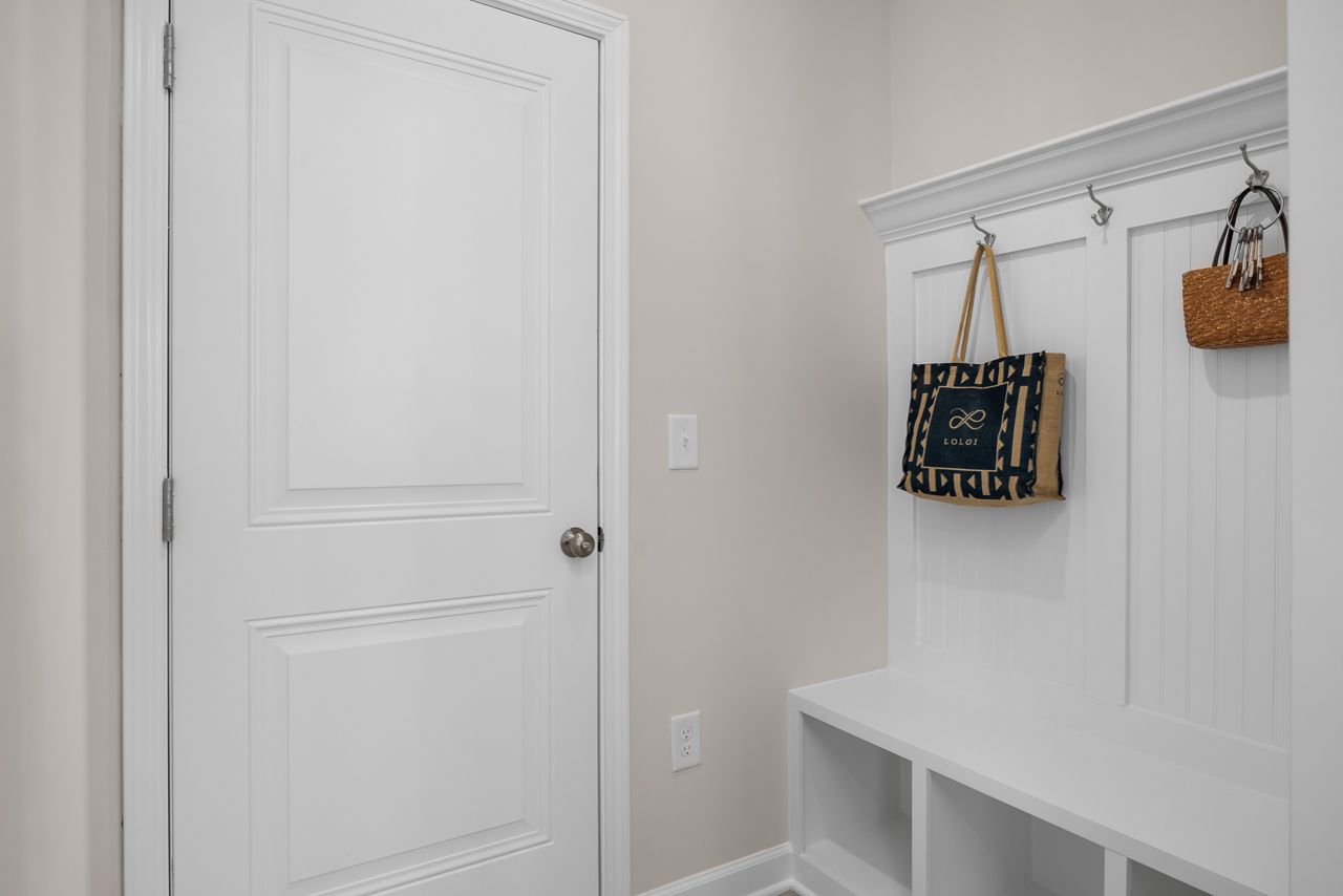 White mudroom drop zone in The Chestnut home design featuring built-in bench seating, storage cubbies, and coat hooks.