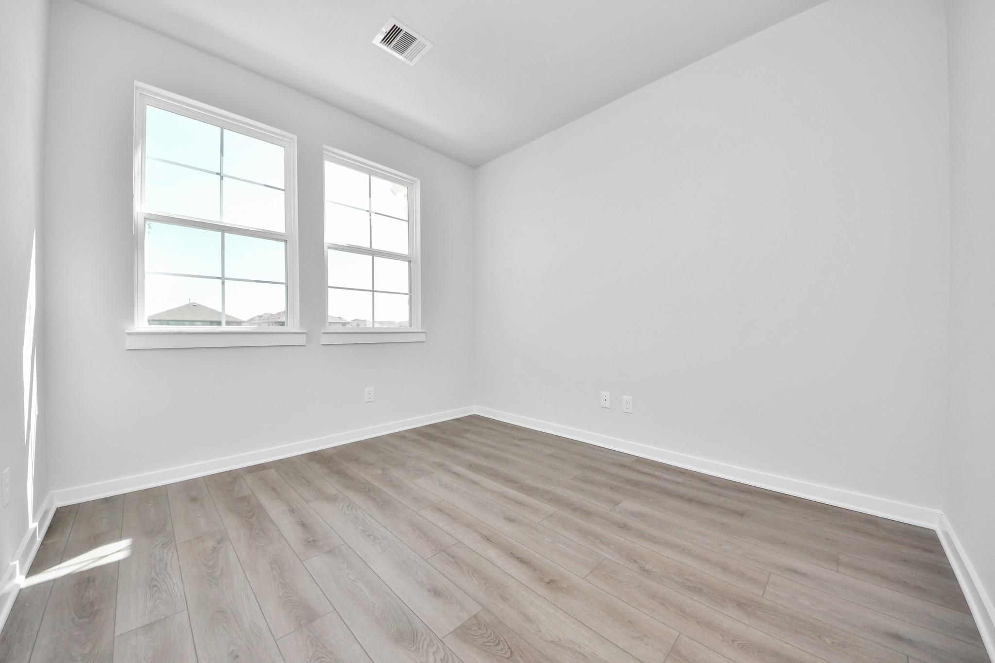 Bright, spacious secondary bedroom with wood-look flooring in The Riviera A floor plan at Emberly in Beasley, Texas.