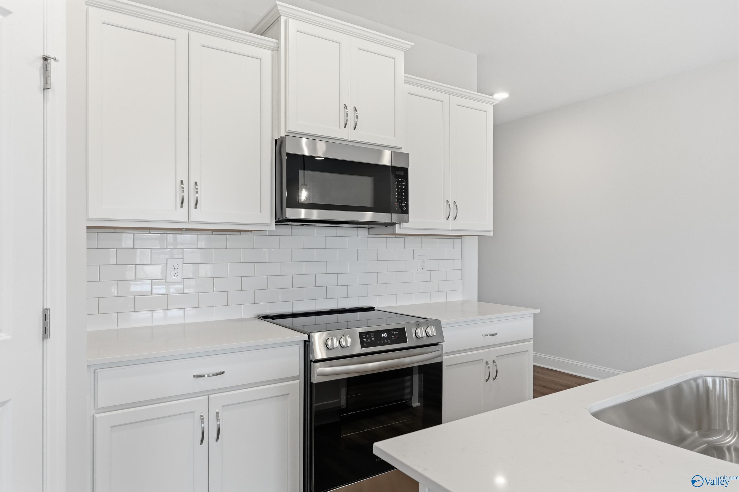 Modern white kitchen featuring stainless steel appliances, subway tile backsplash, and quartz counters in Davidson Homes The Daphne C, Toney, AL