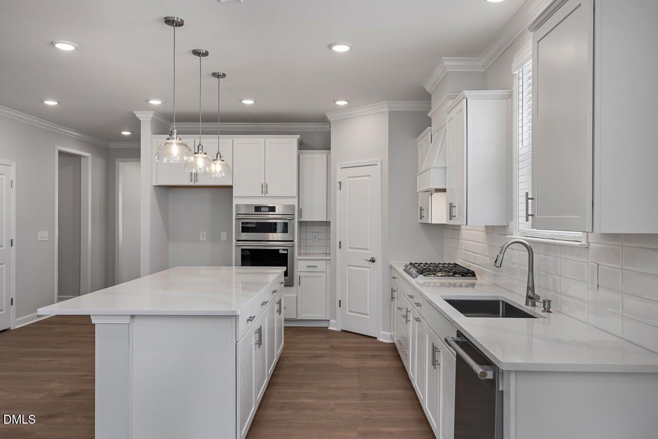 Modern white kitchen with quartz island, stainless steel appliances, and pendant lighting in The Ashport L, Wake Forest, NC.