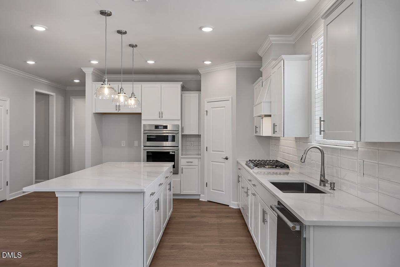 Modern white kitchen with quartz island, stainless steel appliances, and pendant lighting in The Ashport L, Wake Forest, NC.
