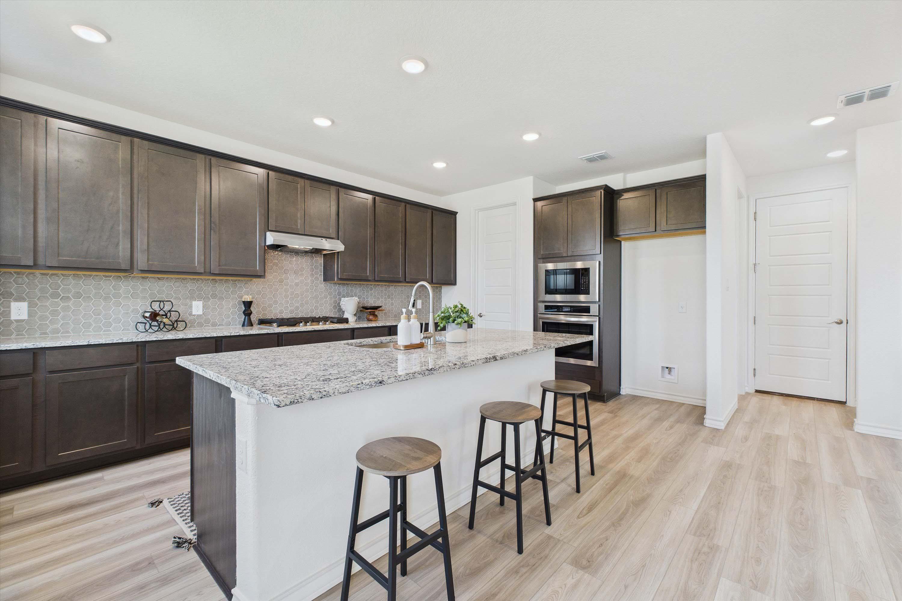 Modern kitchen in The Danbury featuring dark cabinetry, granite island, stainless steel appliances, and wood-style flooring.