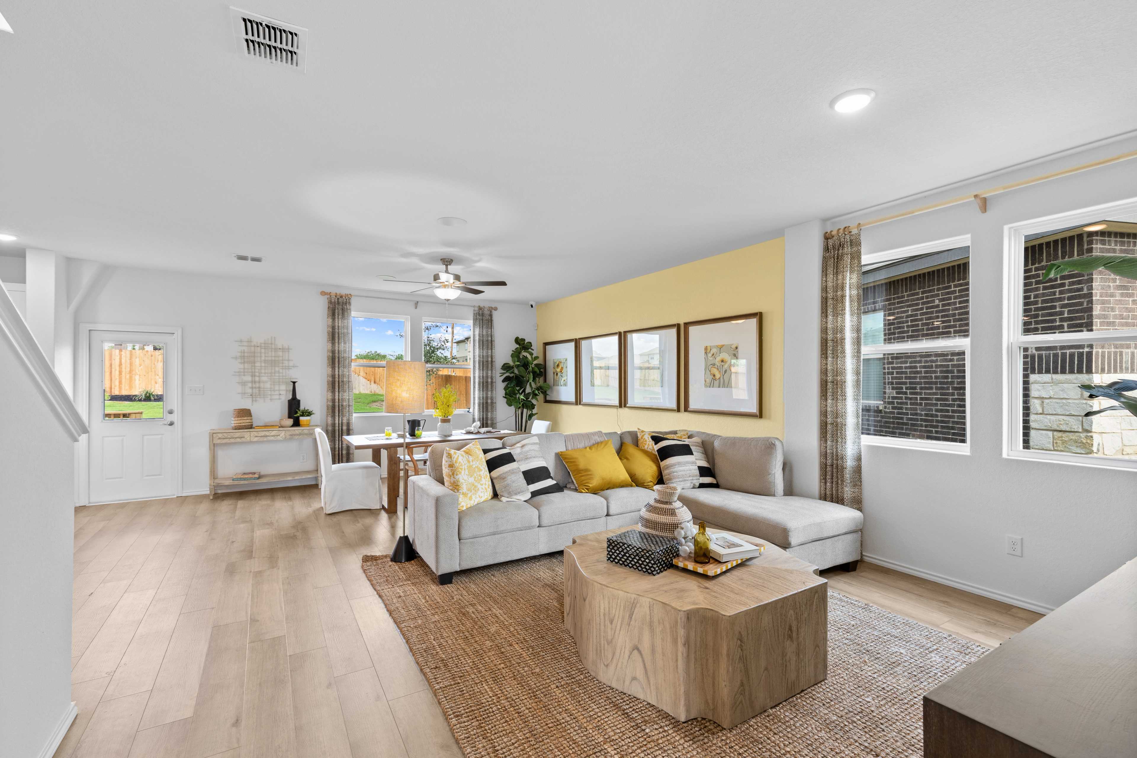 Open-concept living room at Horizon Pointe in Converse TX with gray sectional sofa, yellow accent wall, hardwood floors, and wooden coffee table