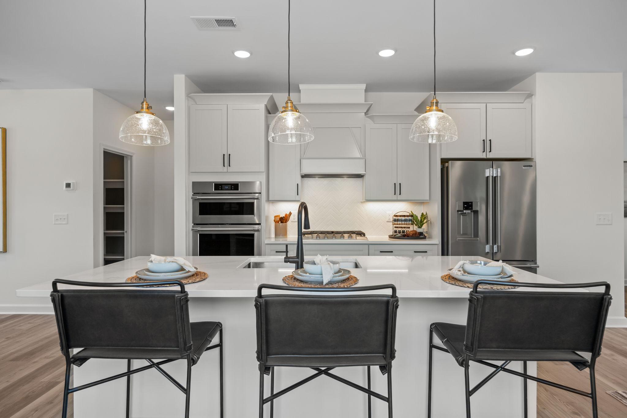 Modern white kitchen in Camden Park Knightdale NC with large island, stainless appliances, pendant lights and black bar stools