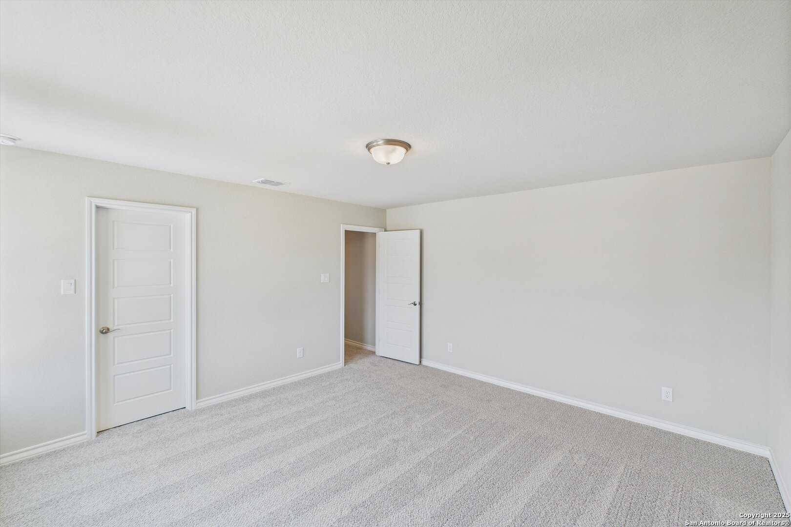Empty secondary bedroom with beige walls, neutral striped carpet, and double doors in Davidson Homes The Jennings H, Ladera, San Antonio