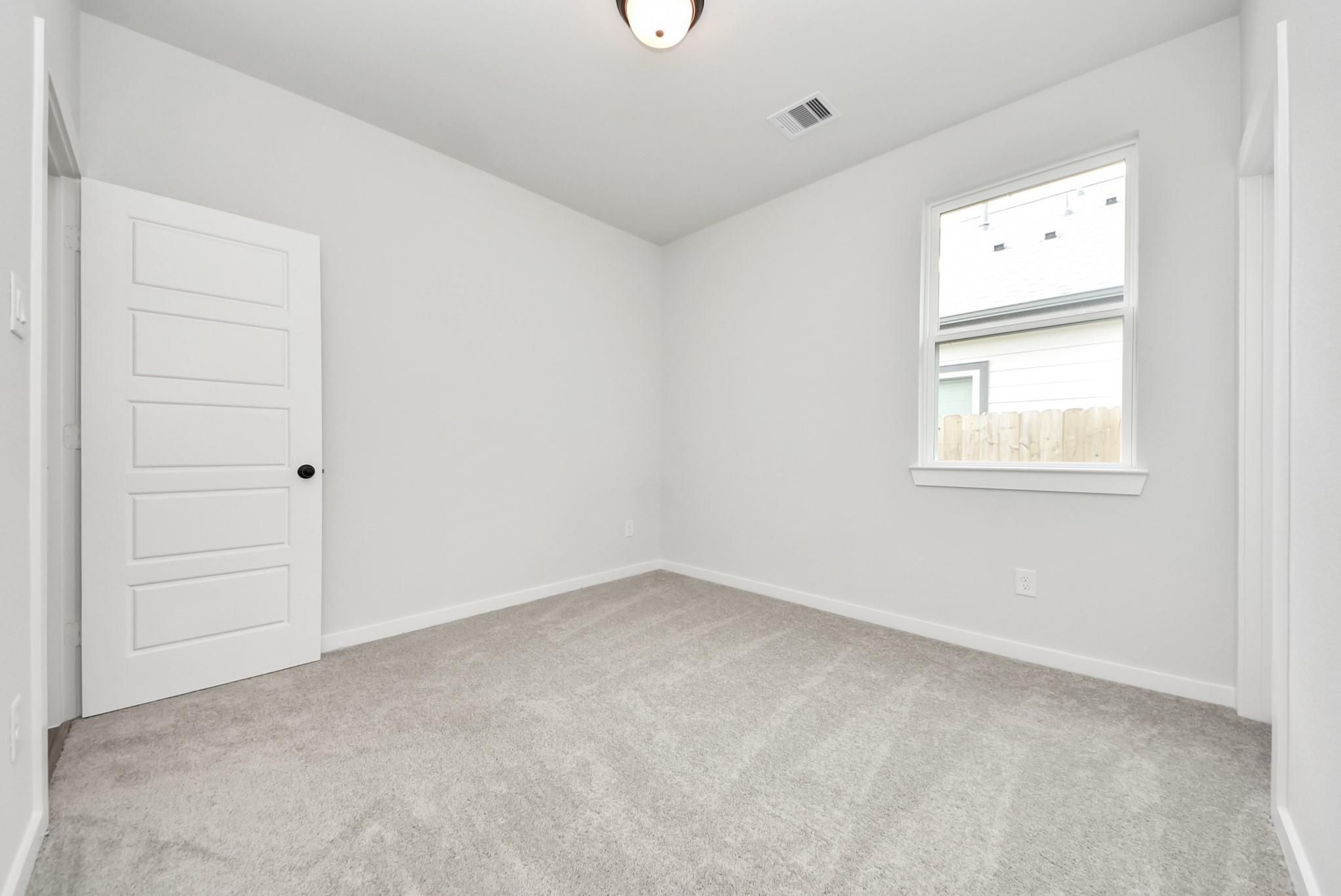 Bright, carpeted spare bedroom with white walls in The Daphne F floor plan at Sundance Cove, Crosby, Texas.